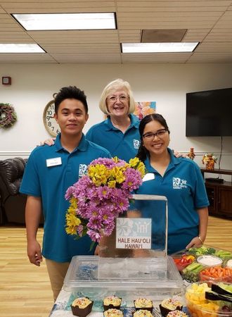 A group of people standing around a table with cupcakes and flowers.