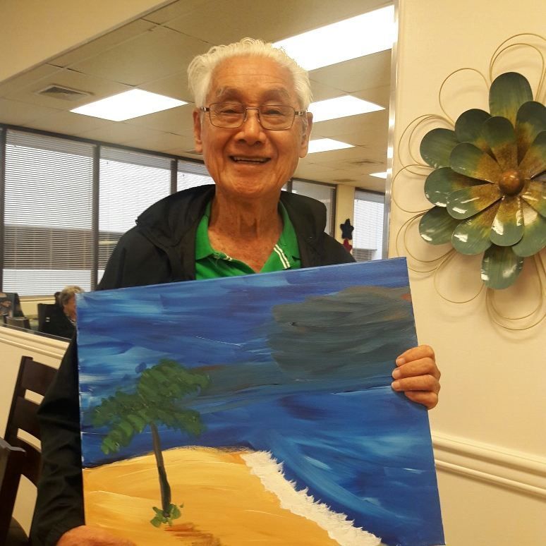 An elderly man is holding a painting of a beach scene