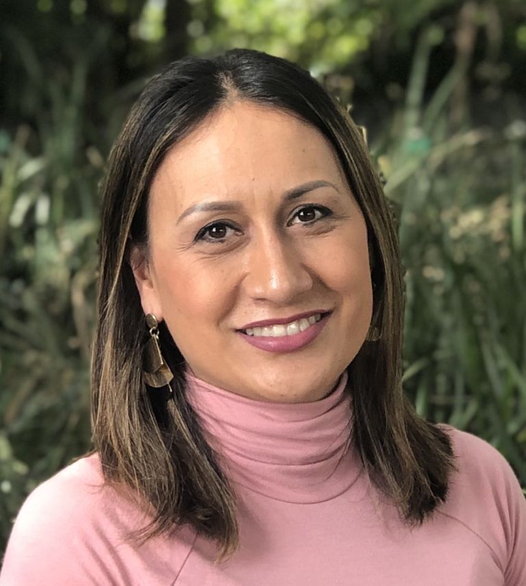 A woman in a pink turtleneck is smiling for the camera.
