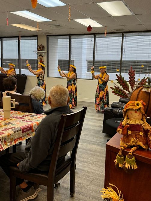 A group of elderly people are sitting at a table watching a hula performance.