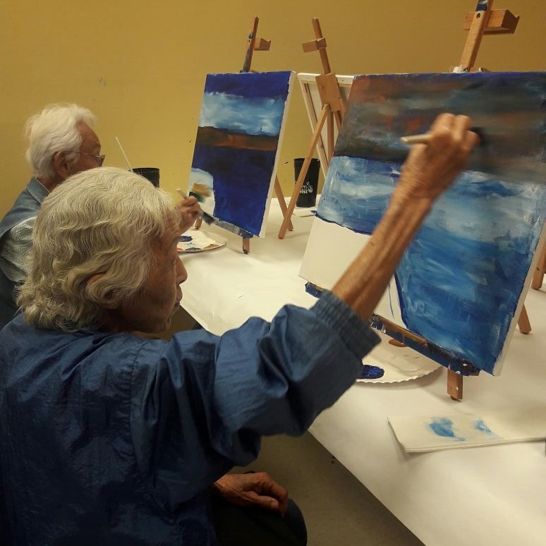 A man is painting a picture of the ocean on an easel