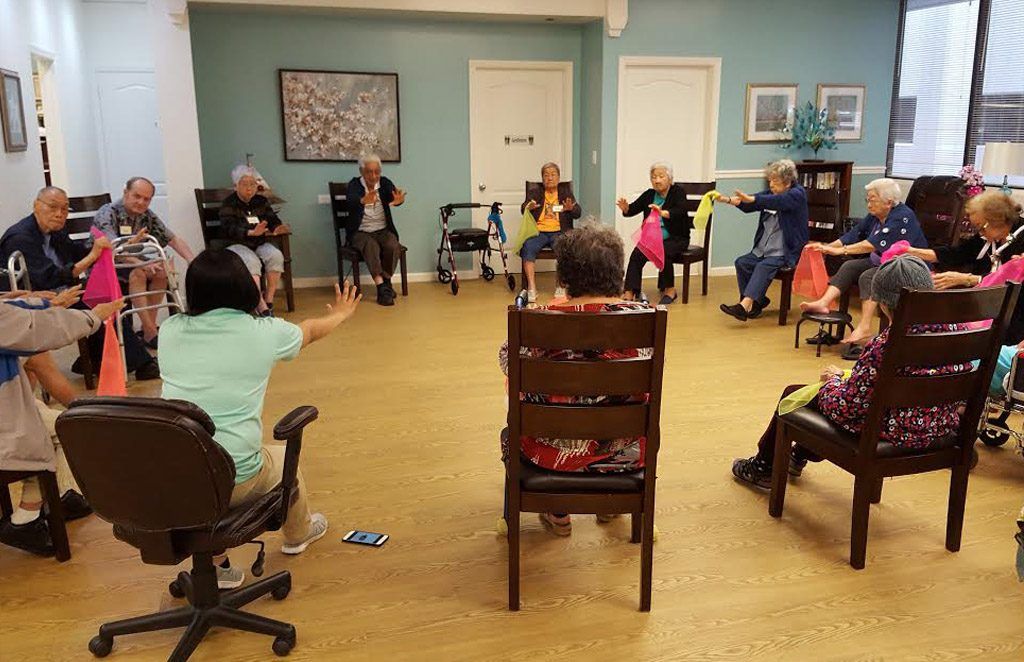A group of elderly people are sitting in chairs in a circle doing exercises.