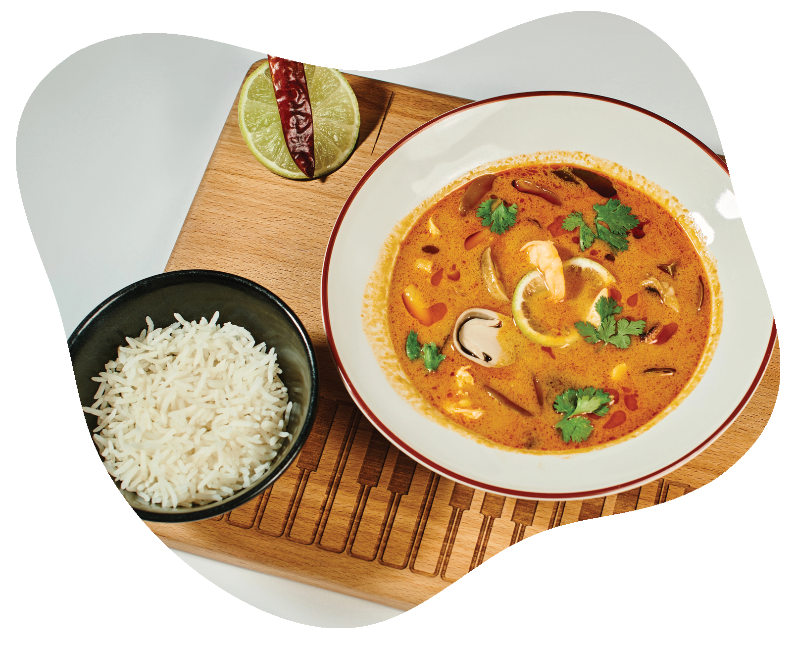 A bowl of soup next to a bowl of rice on a wooden cutting board.