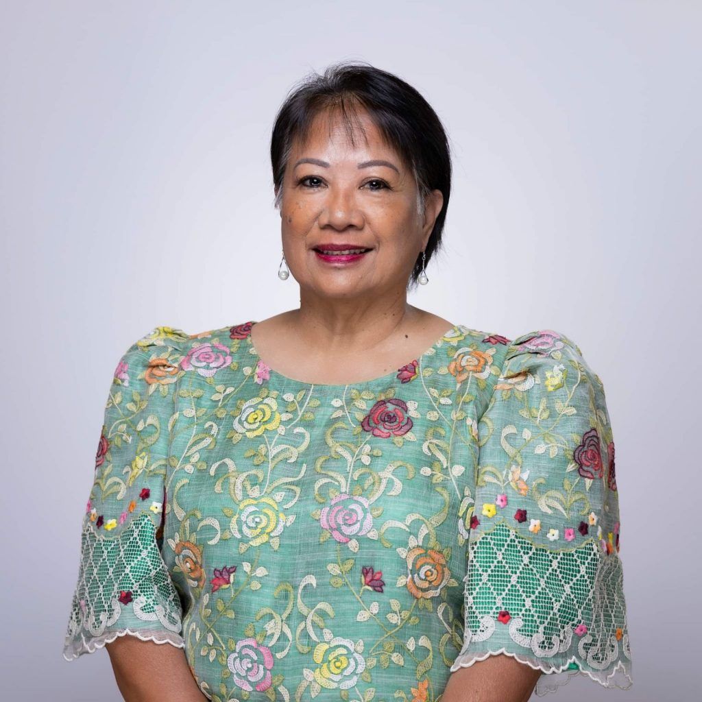 A woman in a green floral dress is smiling for the camera.