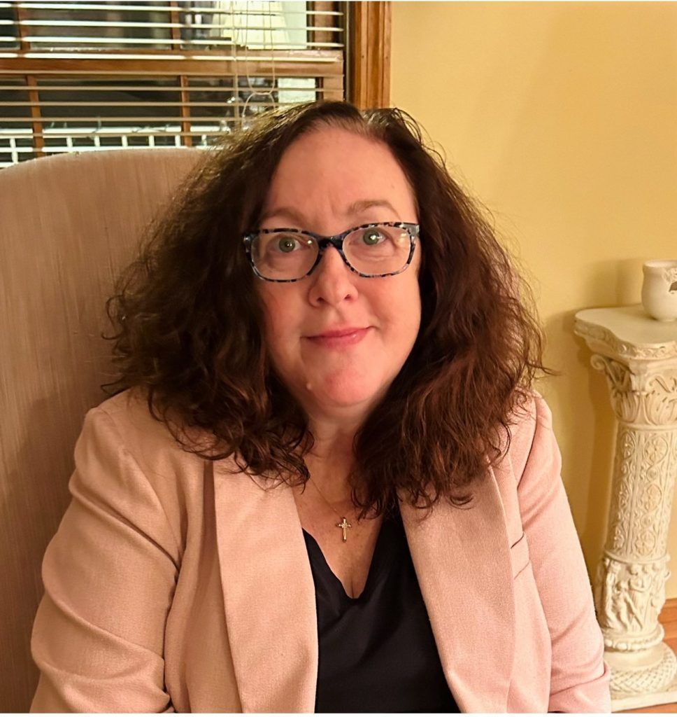 A woman wearing glasses and a pink jacket is sitting in a chair