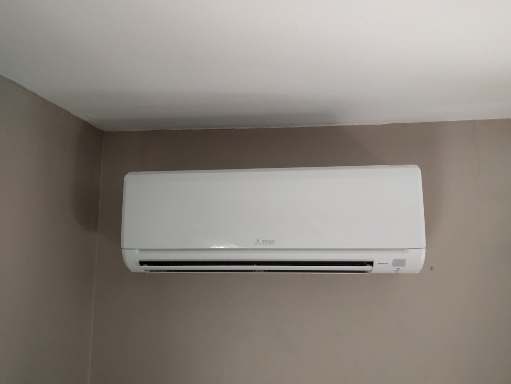 White wall-mounted air conditioner on a tan wall in the corner of a room.