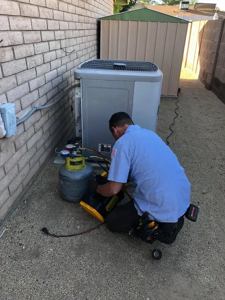 HVAC technician working on an air conditioner unit outside a building, using tools and a yellow tank.