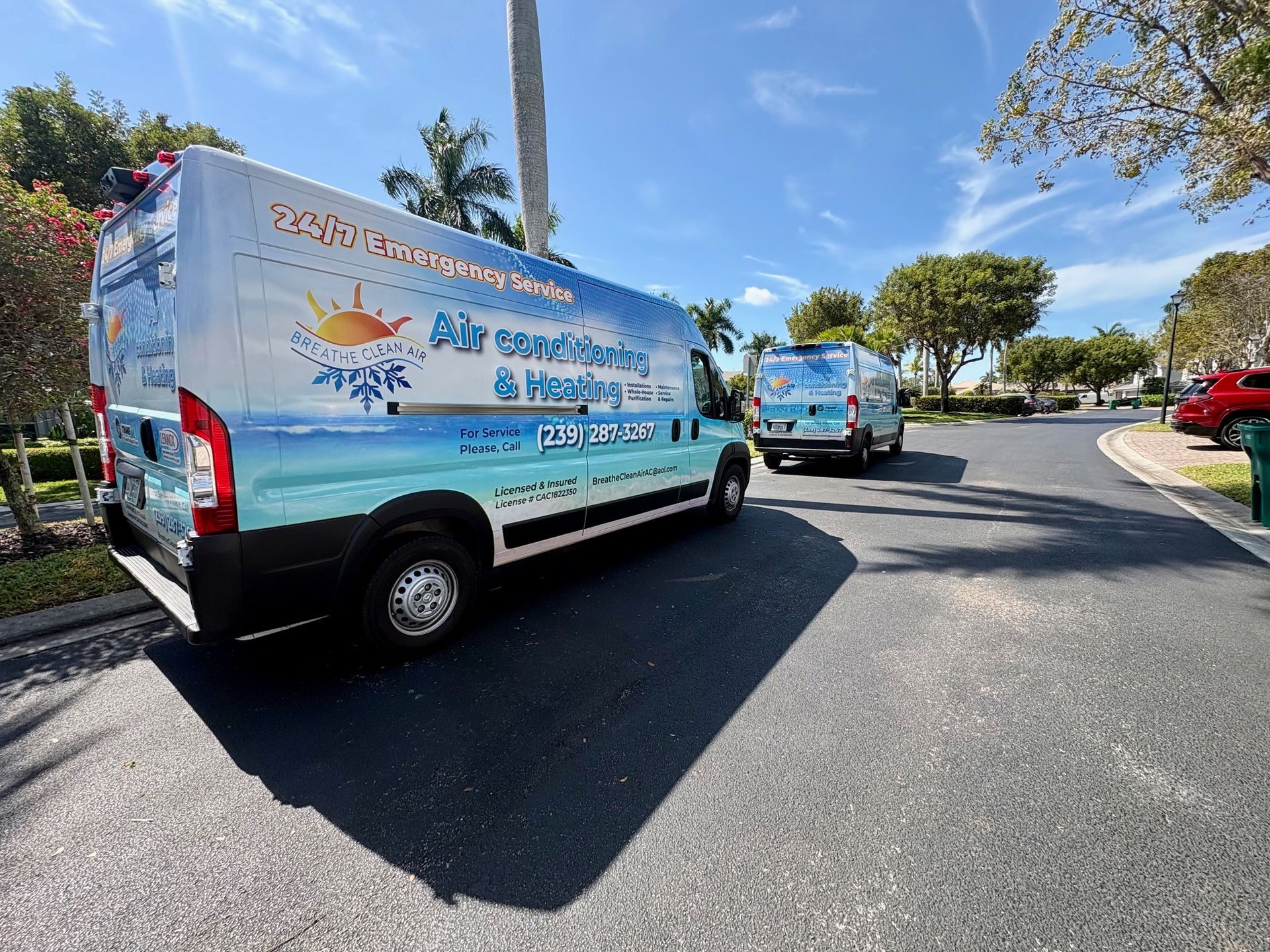 Two air conditioning service vans parked on asphalt street under a blue sky.