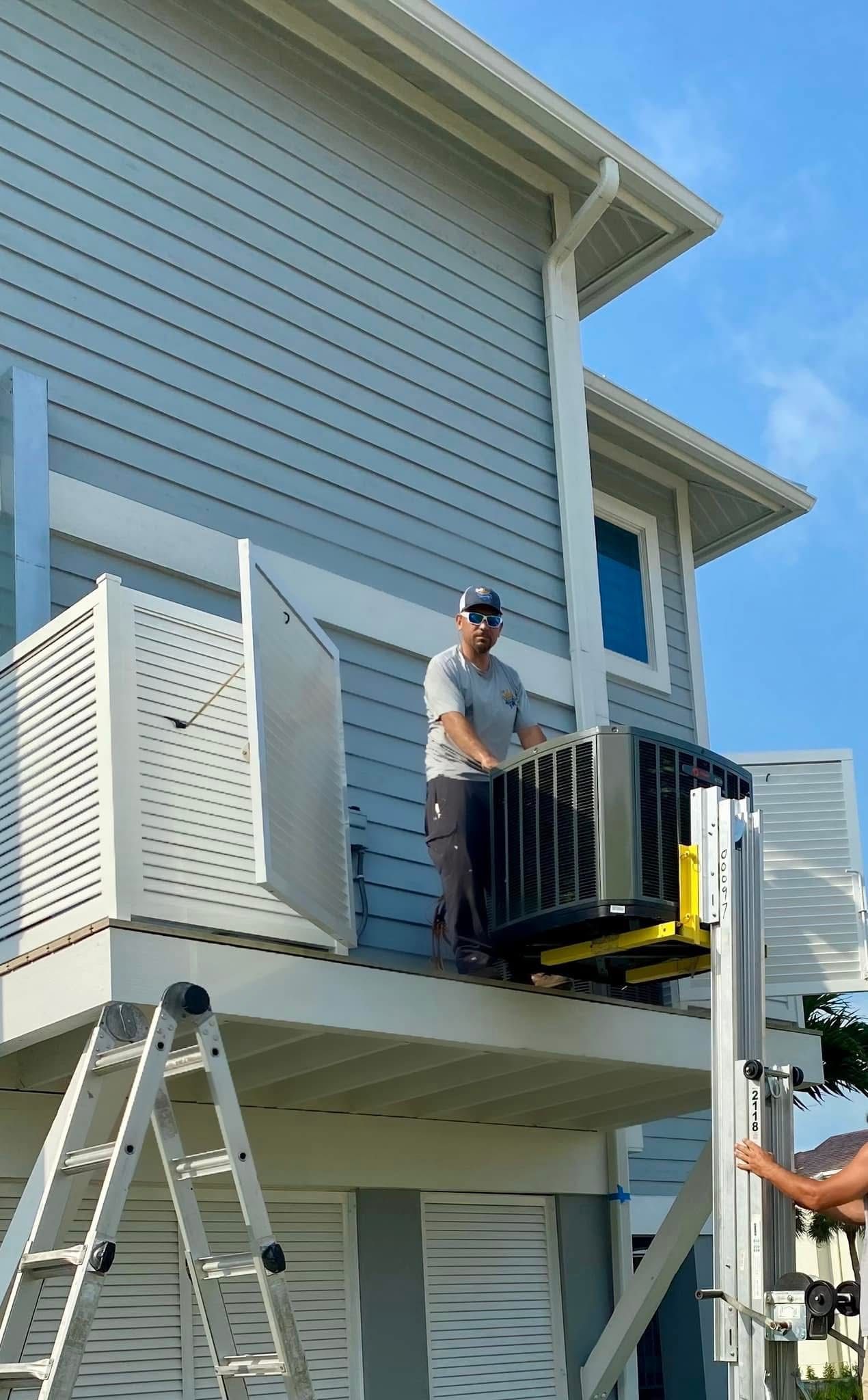 Man on a deck, with an appliance in a lift, near a house. White and blue house with a ladder.