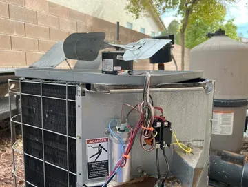 Damaged outdoor HVAC unit with exposed wiring, near a pool pump and brick wall.
