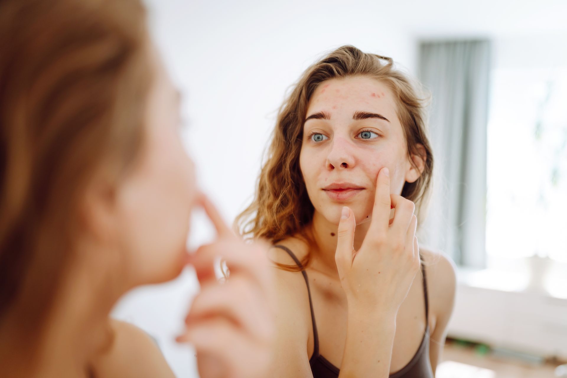 A woman is looking at her face in the mirror.