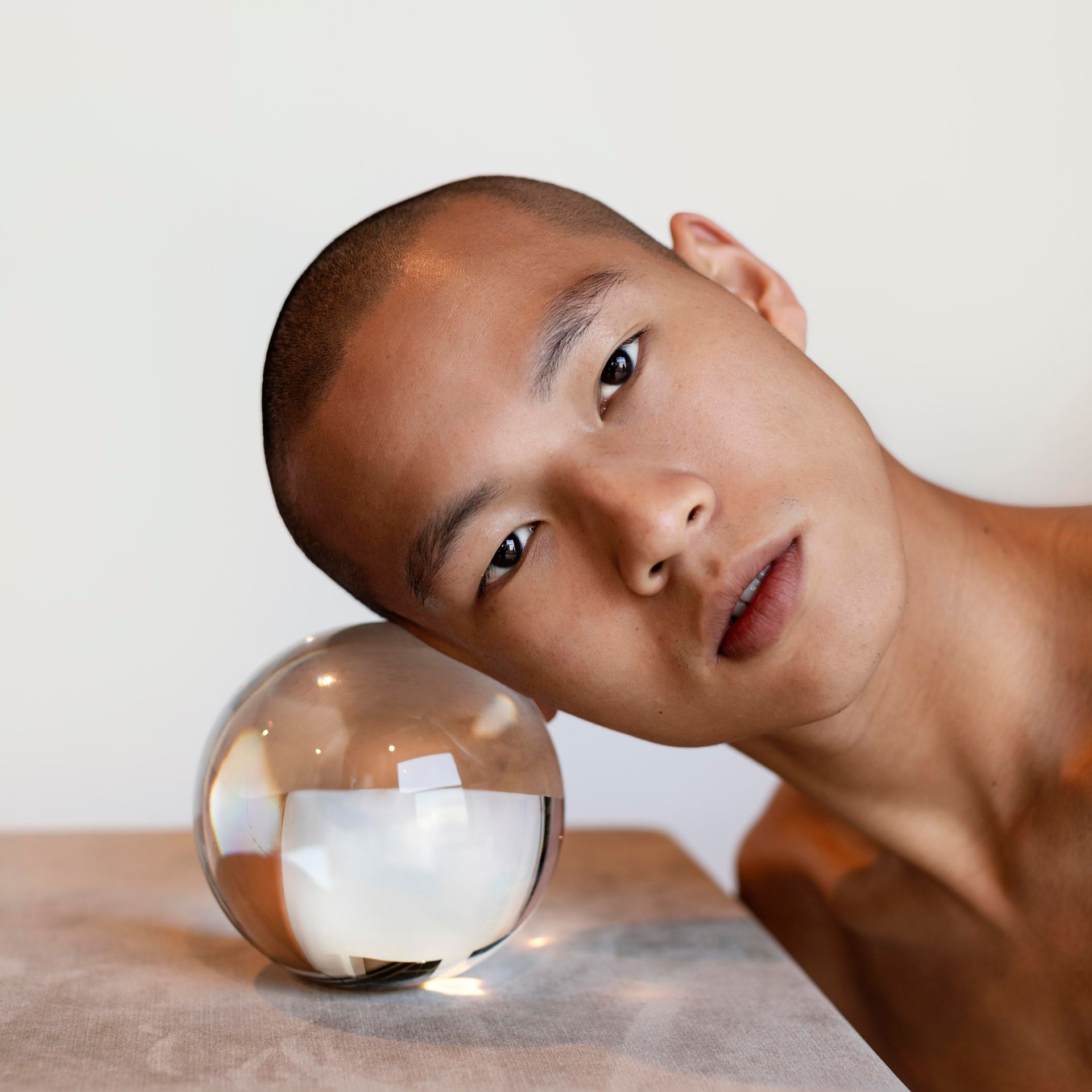 man with great skin resting cheek on glass ball