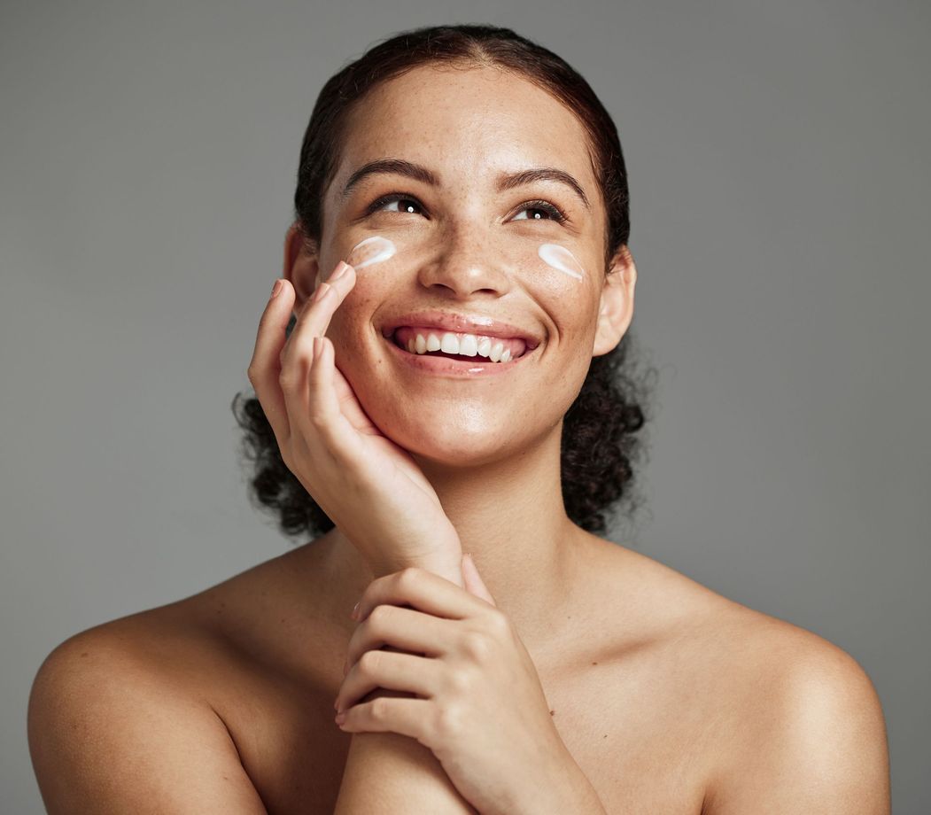 A woman is smiling while applying cream to her face.