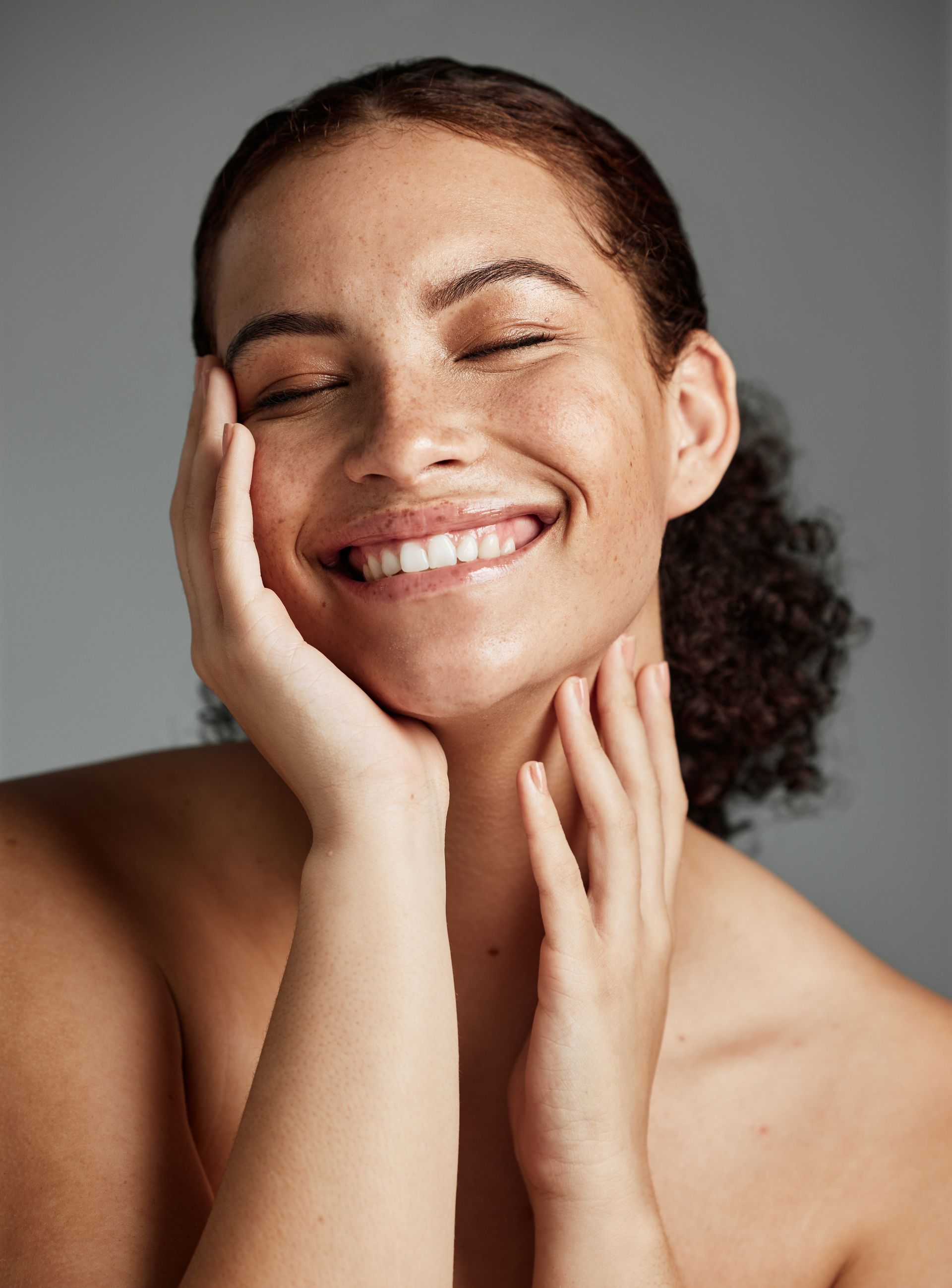 A woman is smiling and touching her face with her hands.