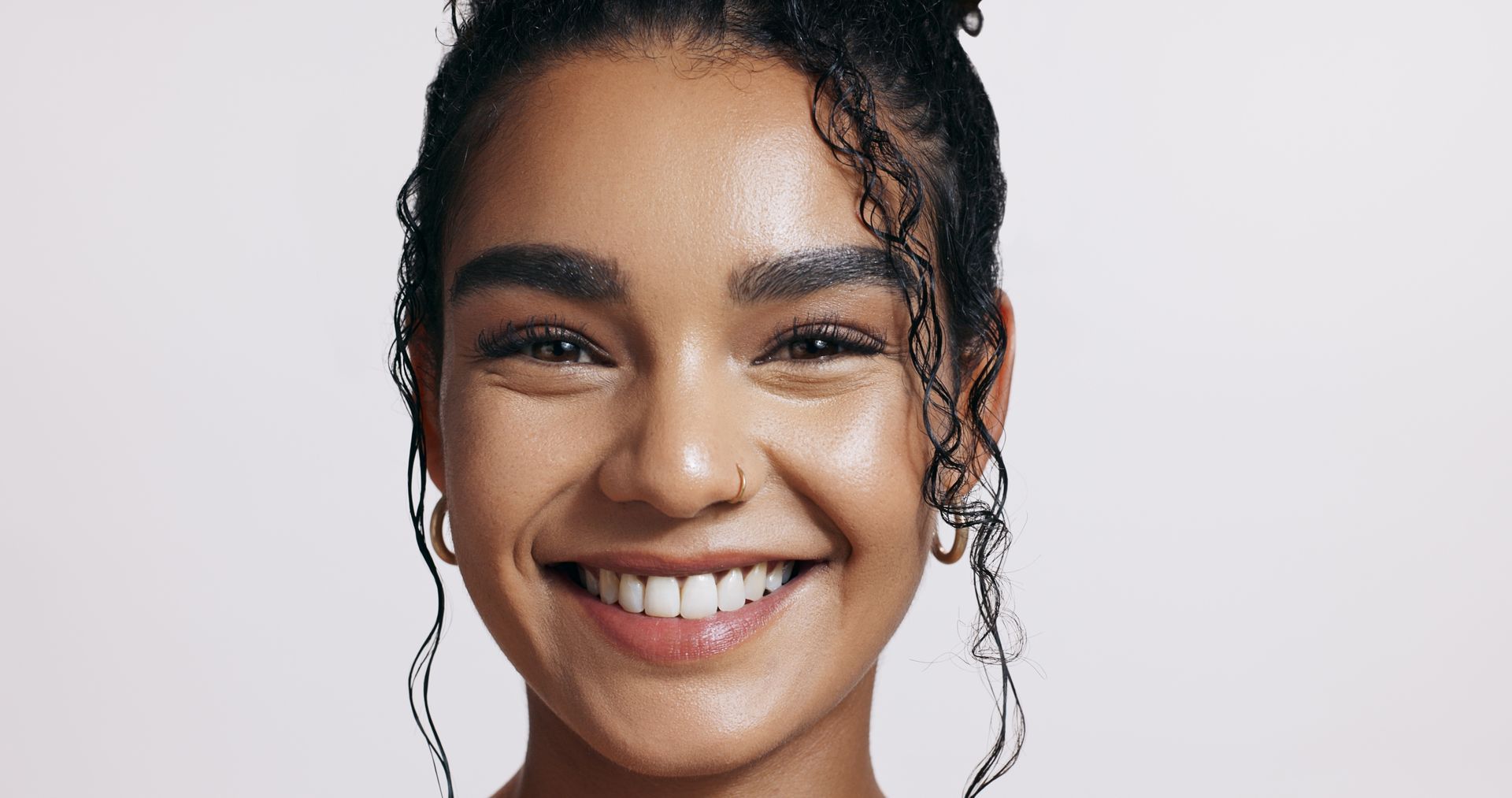 A woman with curly hair is smiling and wearing hoop earrings.