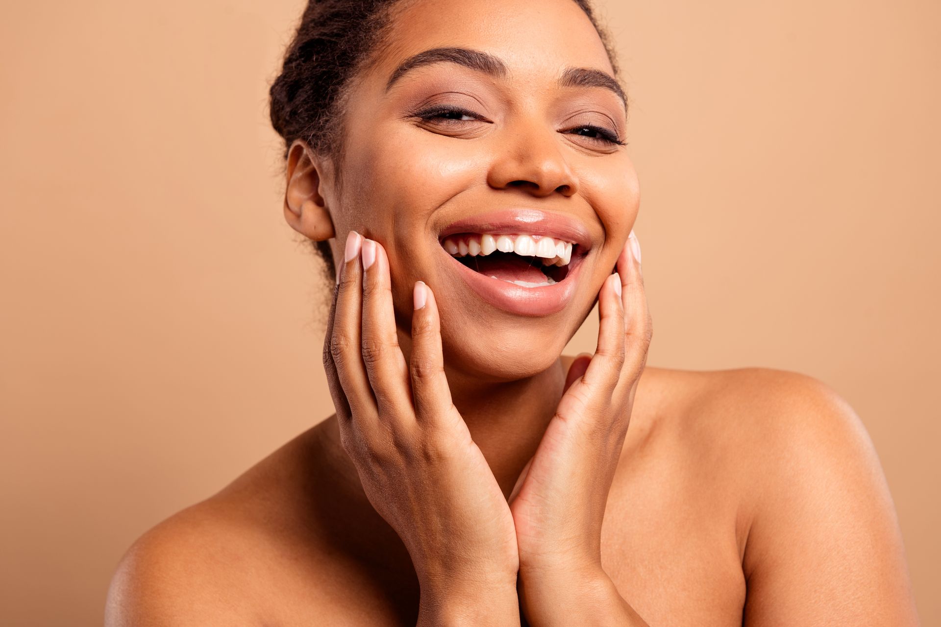 A woman is smiling and touching her face with her hands.