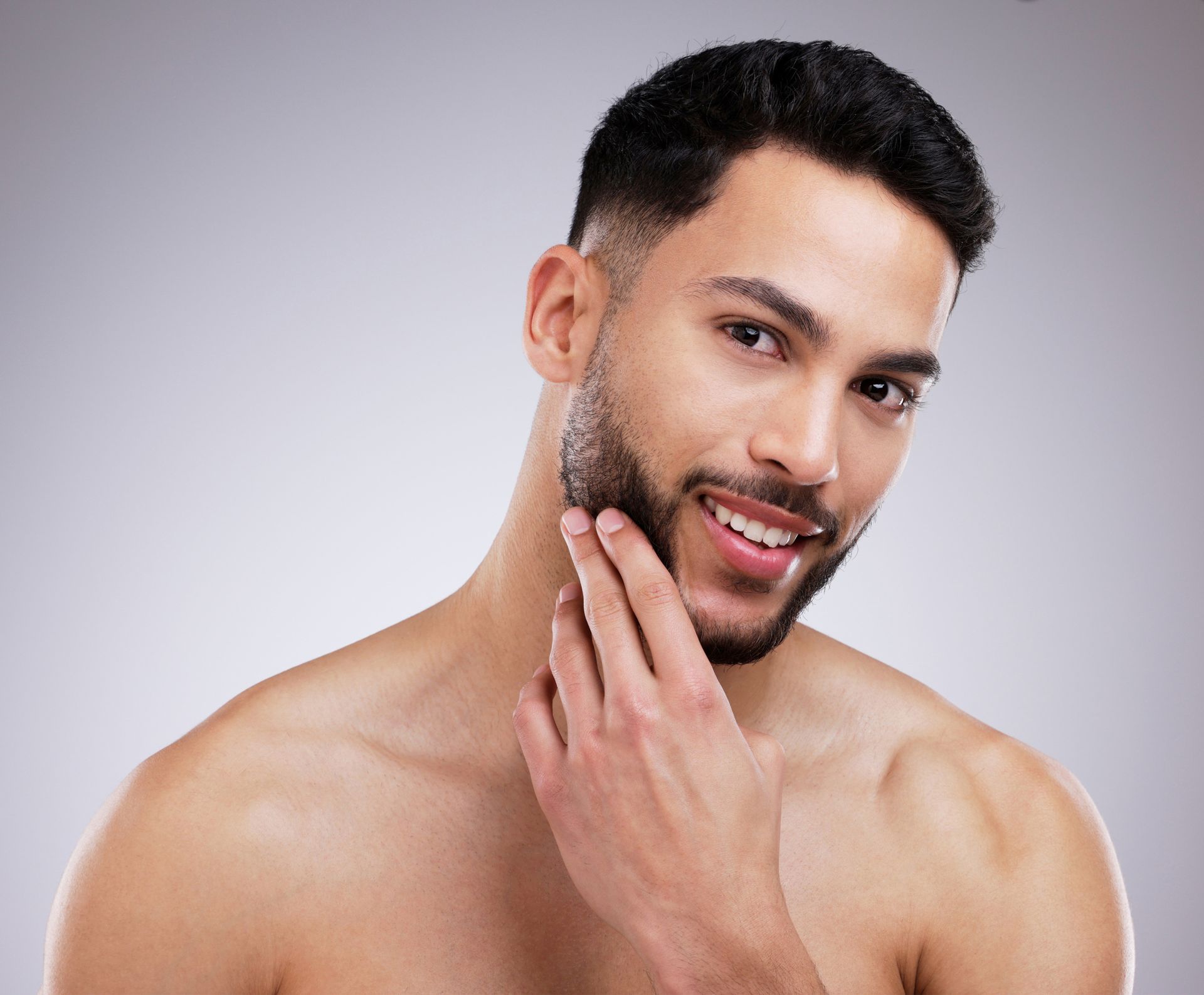 A shirtless man with a beard is shaving his face.