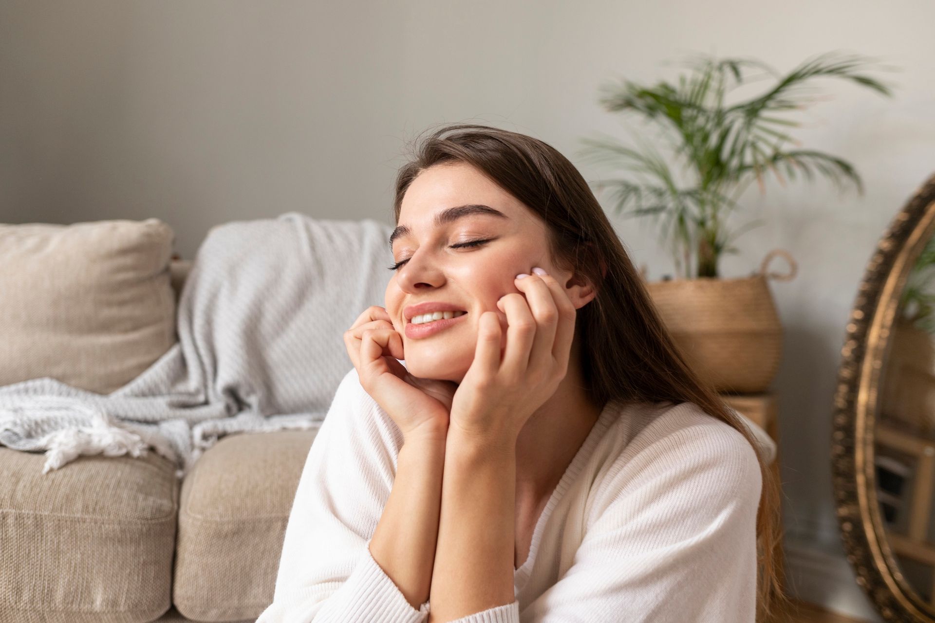 A woman is sitting on a couch with her eyes closed and her hands on her face.