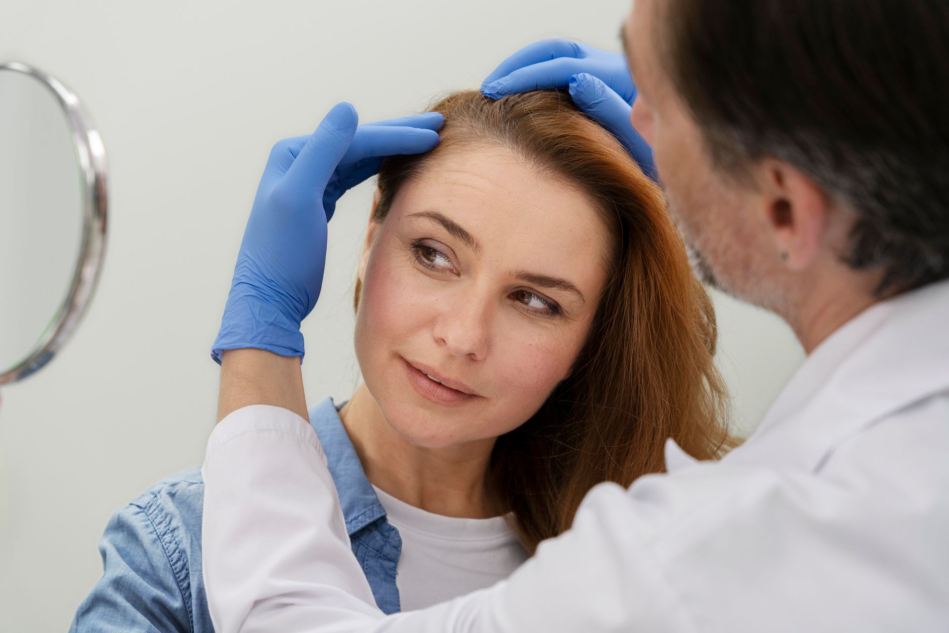 A doctor is examining a woman 's hair in front of a mirror.