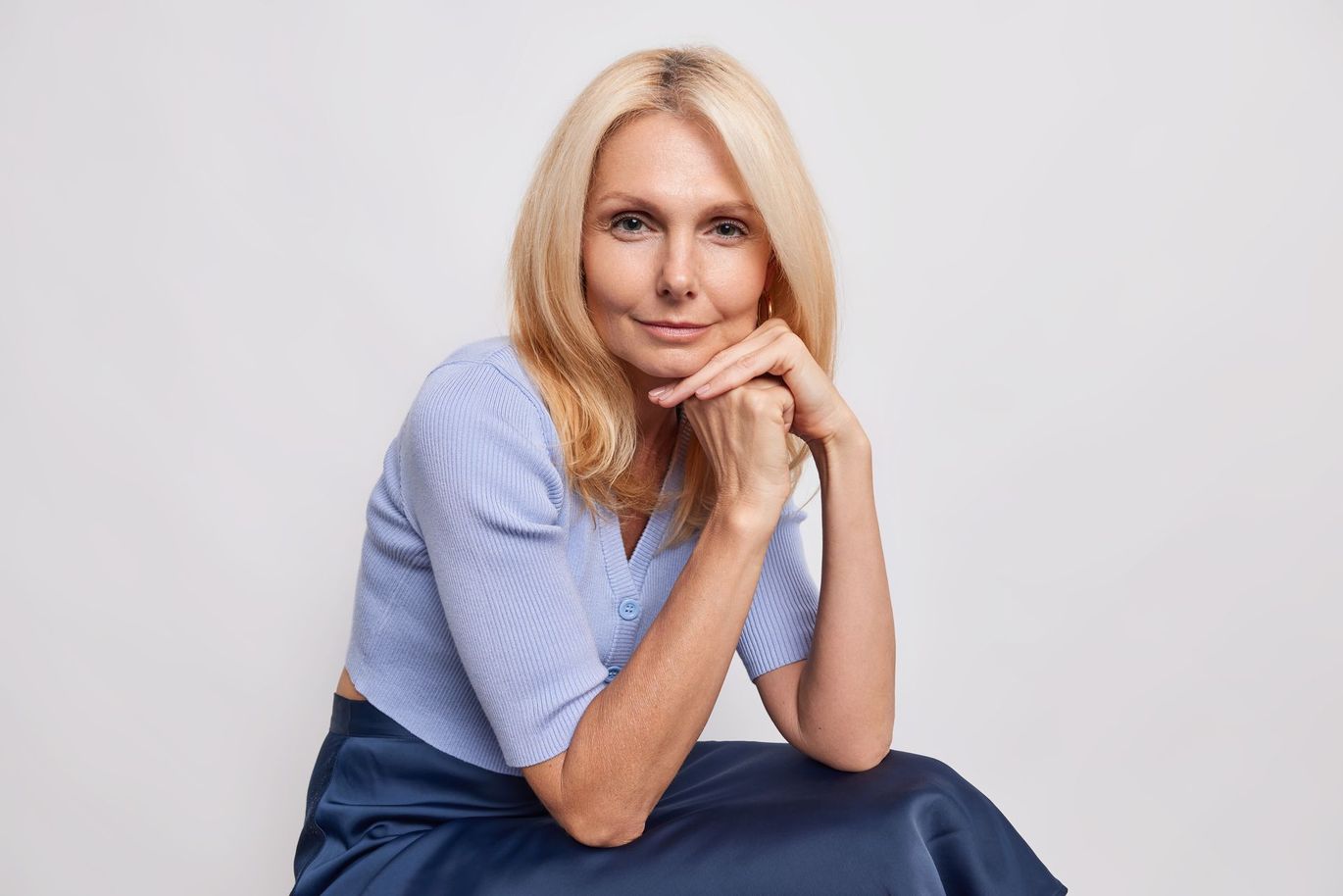 A woman is sitting on the floor with her hands on her chin.