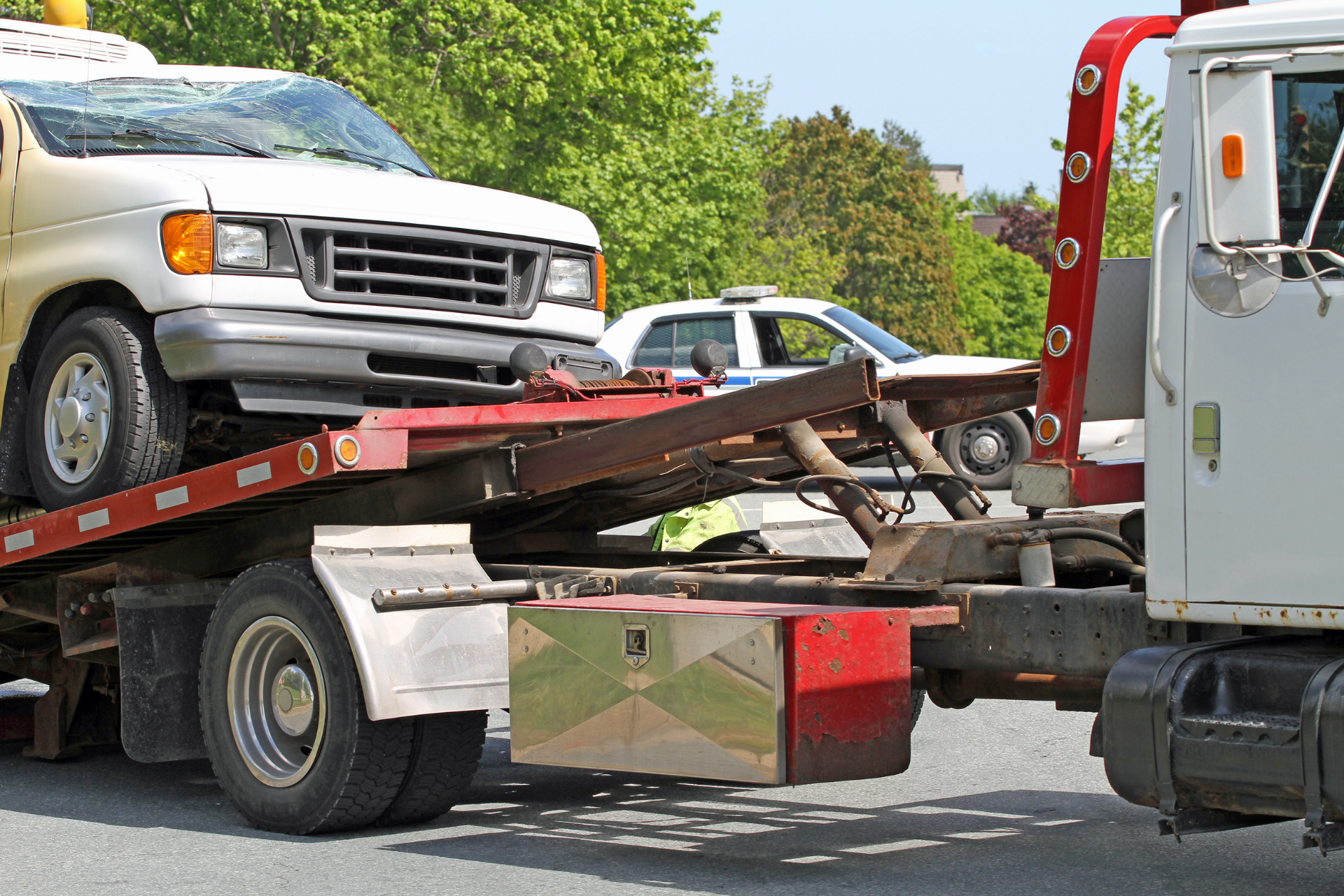 Tow truck towing a white van and car on a road, with damaged front-end vehicles.