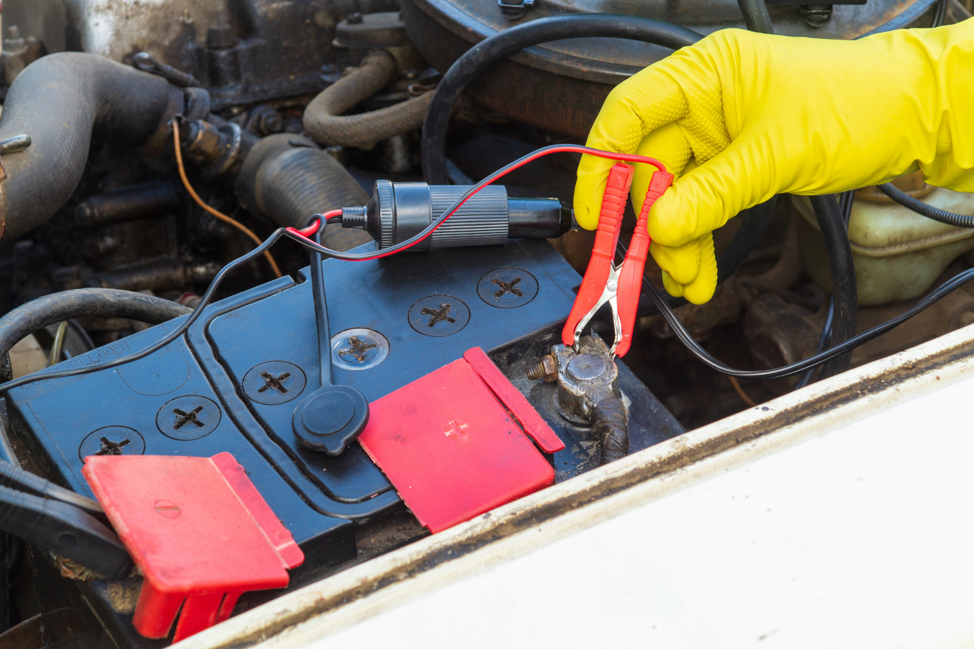 Gloved hand testing a car battery with jumper cables in an engine bay