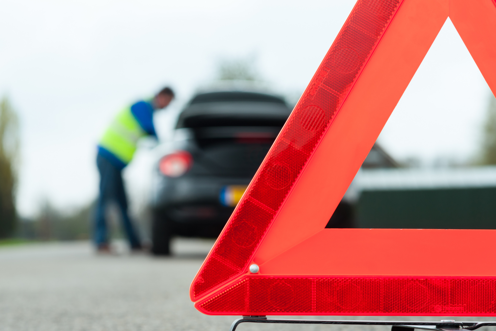 Red warning triangle beside a worker inspecting a car on a roadside breakdown