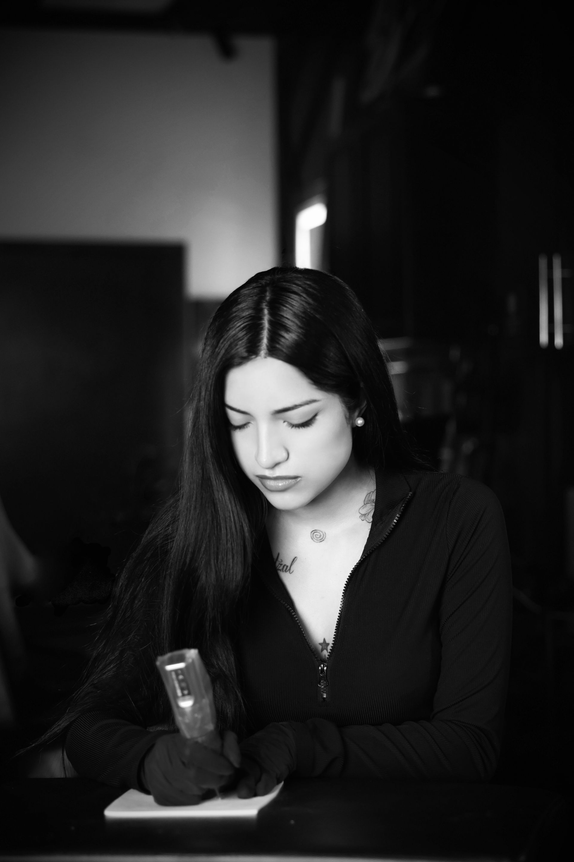 Woman in black shirt tattoos an arm, lit by a studio light.