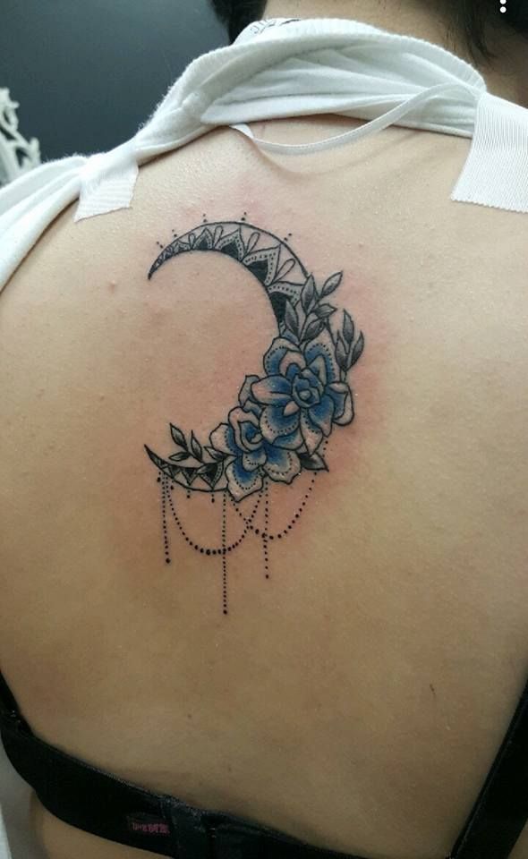 Tattoo of a crescent moon with blue flowers on a person's upper back.