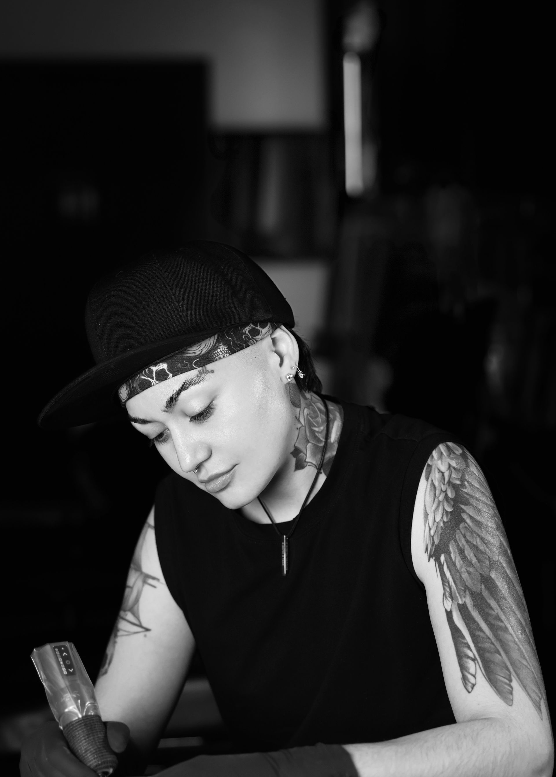 Woman in black shirt tattoos an arm, lit by a studio light.