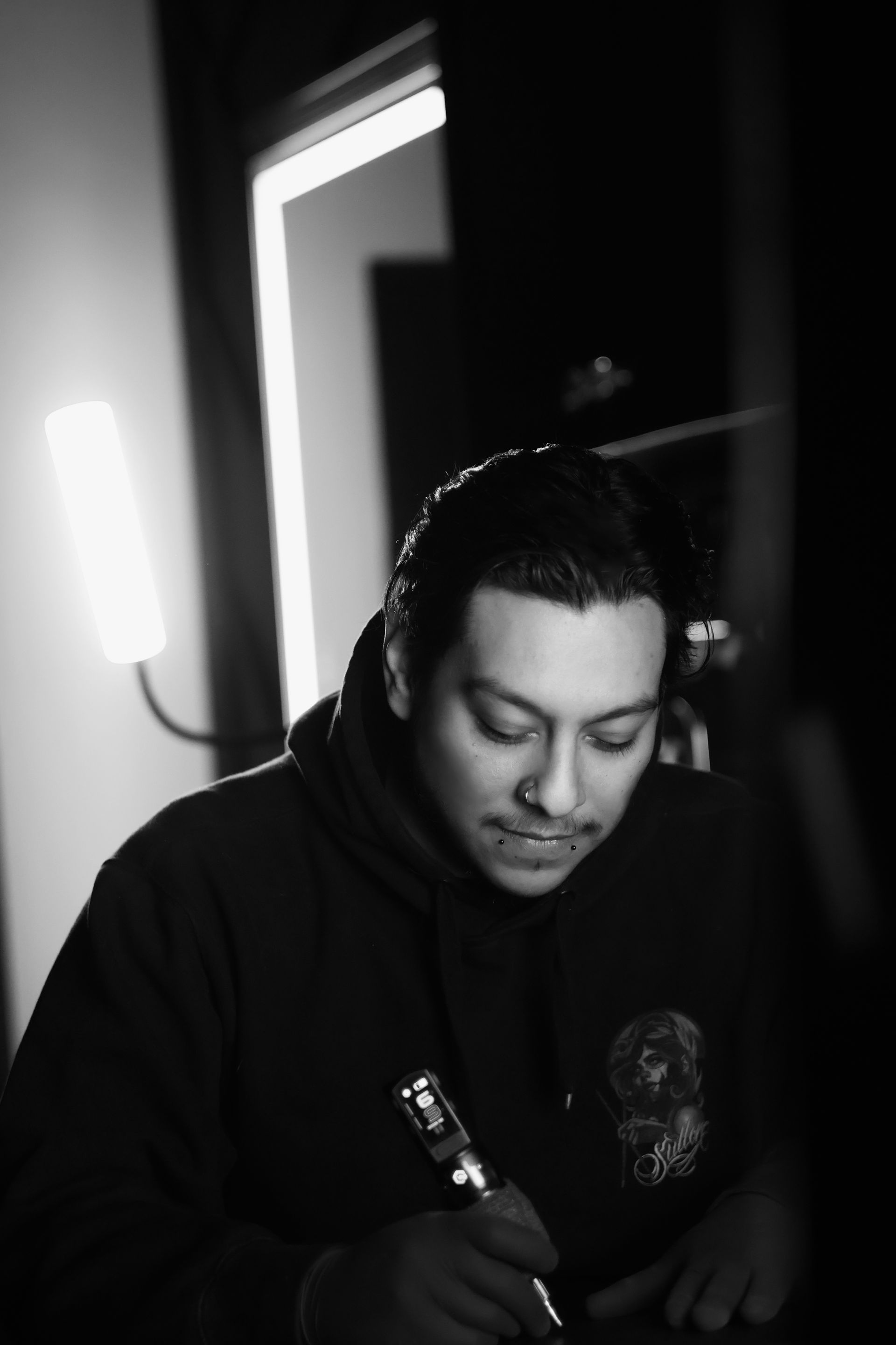 Tattoo artist in a shop, wearing gloves and cap, inking a person's leg. Black and white.