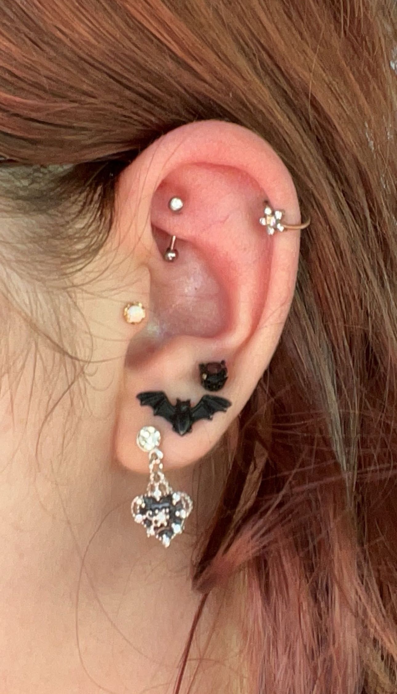 Close-up of an ear with multiple piercings and decorative jewelry, including a bat and flower design.