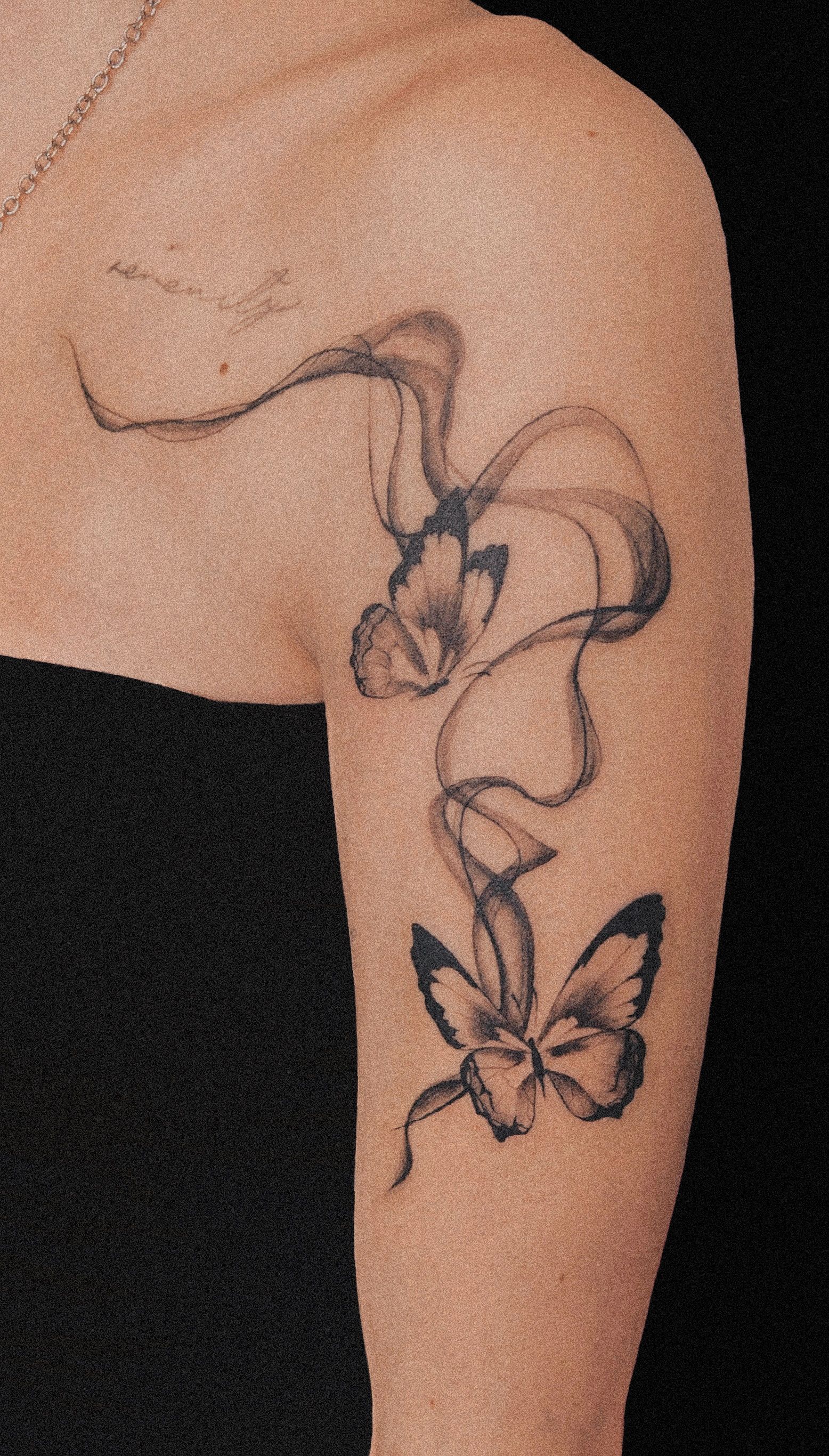 Tattoo of two butterflies and ribbons on a person's arm. The design is black and gray.