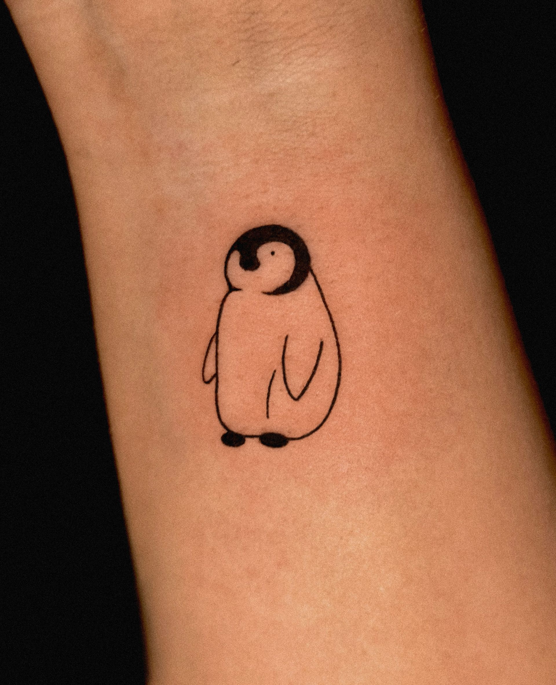 Simple penguin tattoo on a wrist, black outline with black head, simple design.