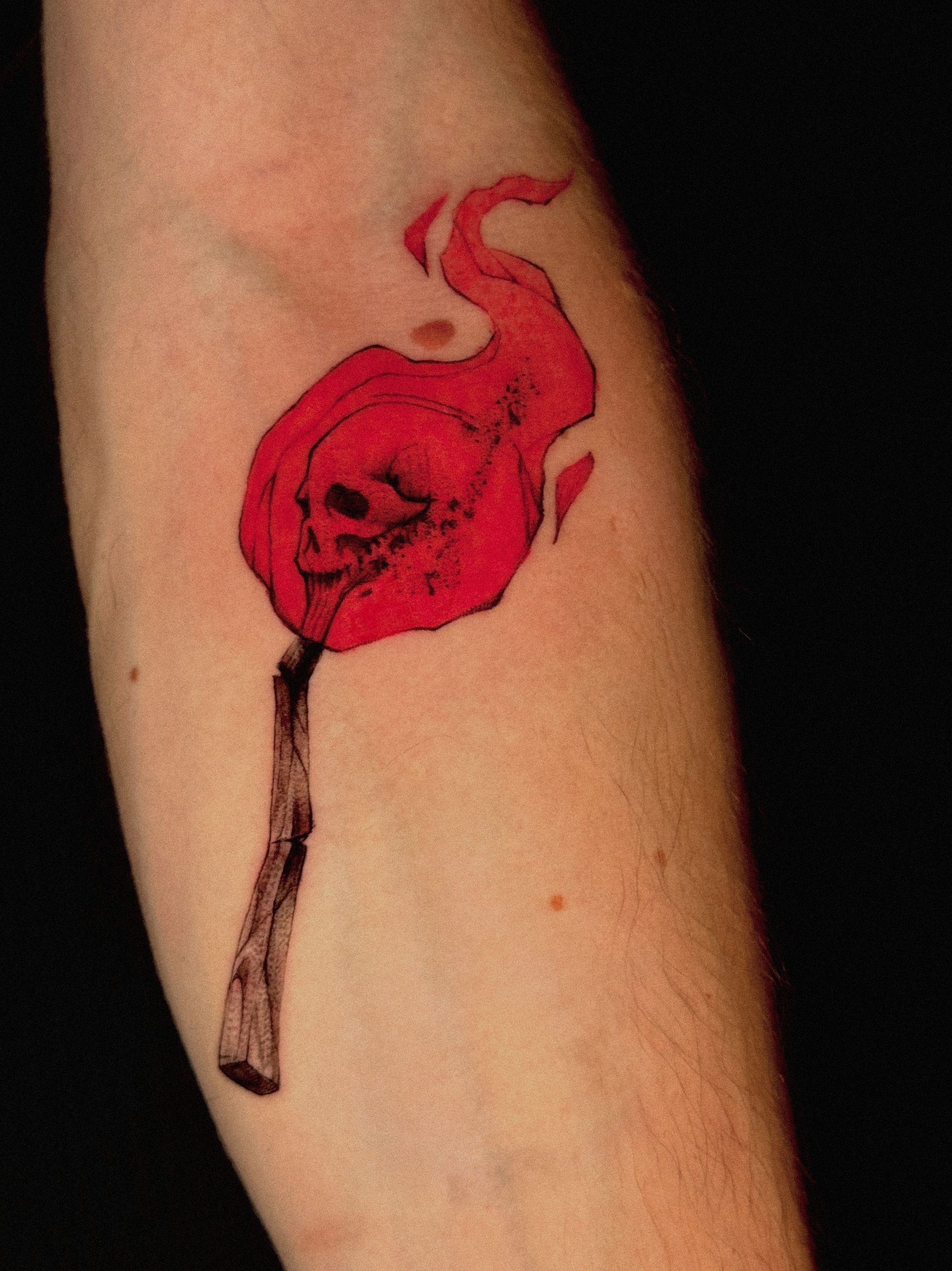 Tattoo of a red skull with flames on a matchstick arm.