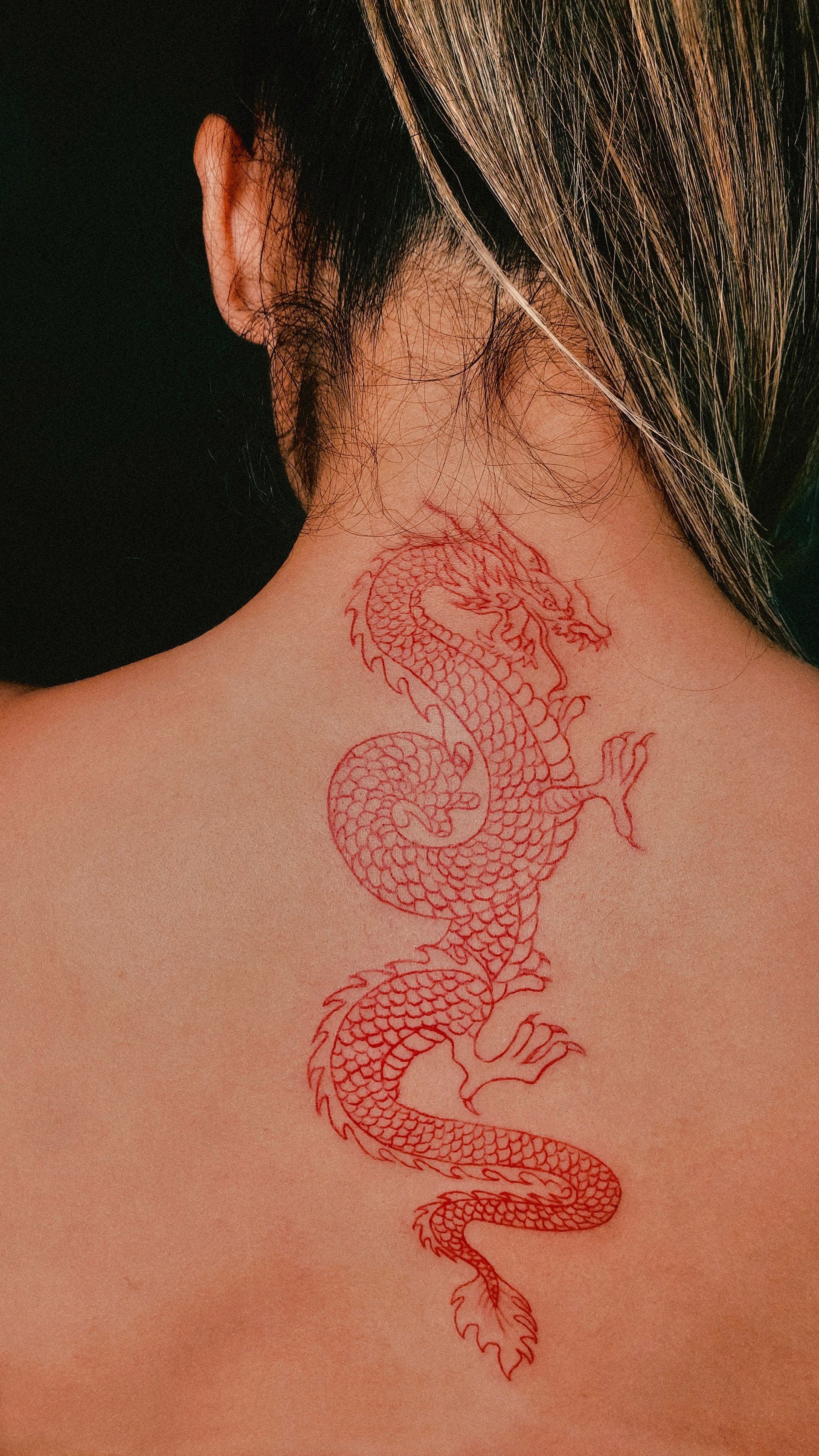 Red dragon tattoo on a person's back, seen from behind.