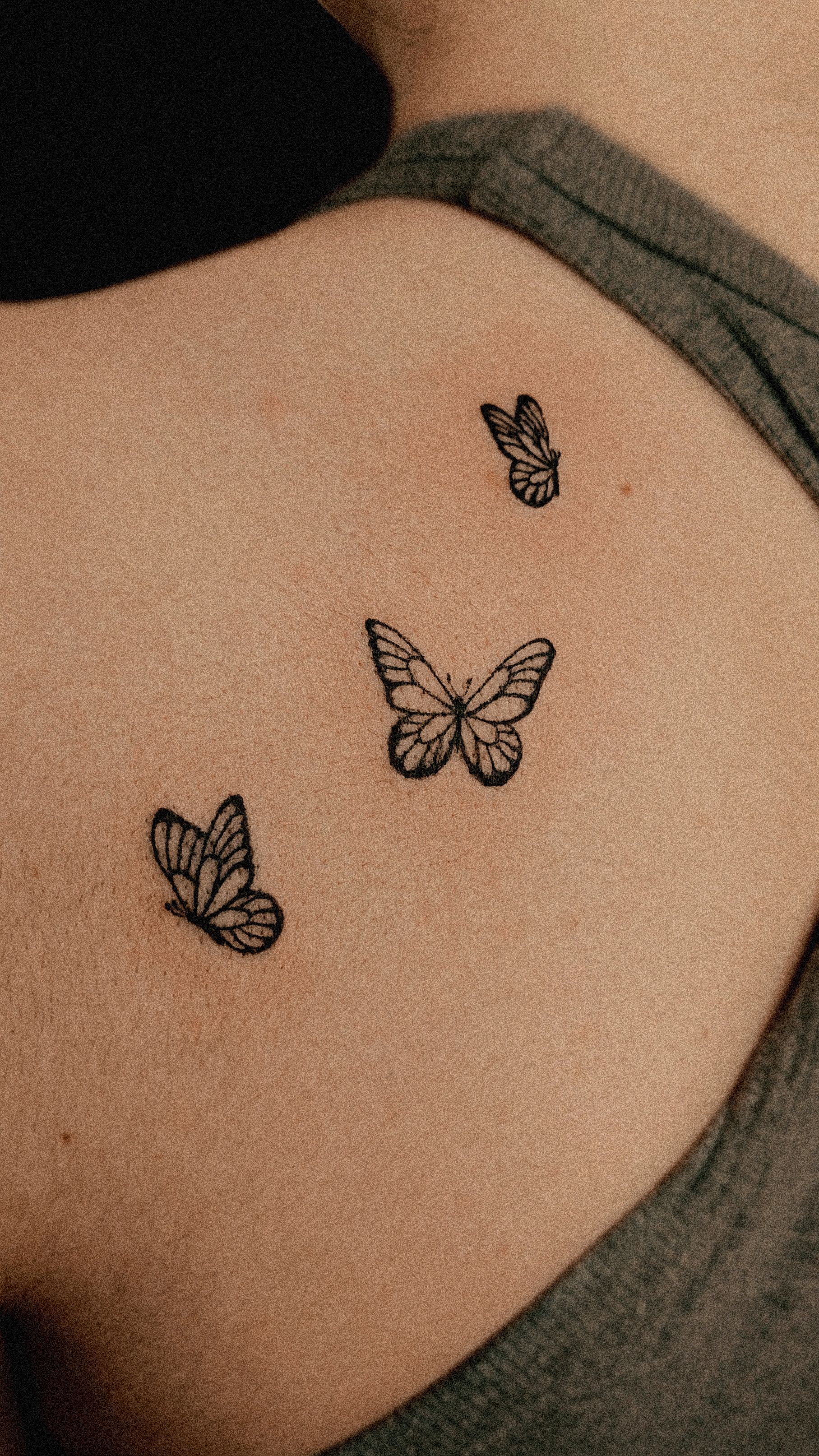 Three small black butterfly tattoos on a person's shoulder.
