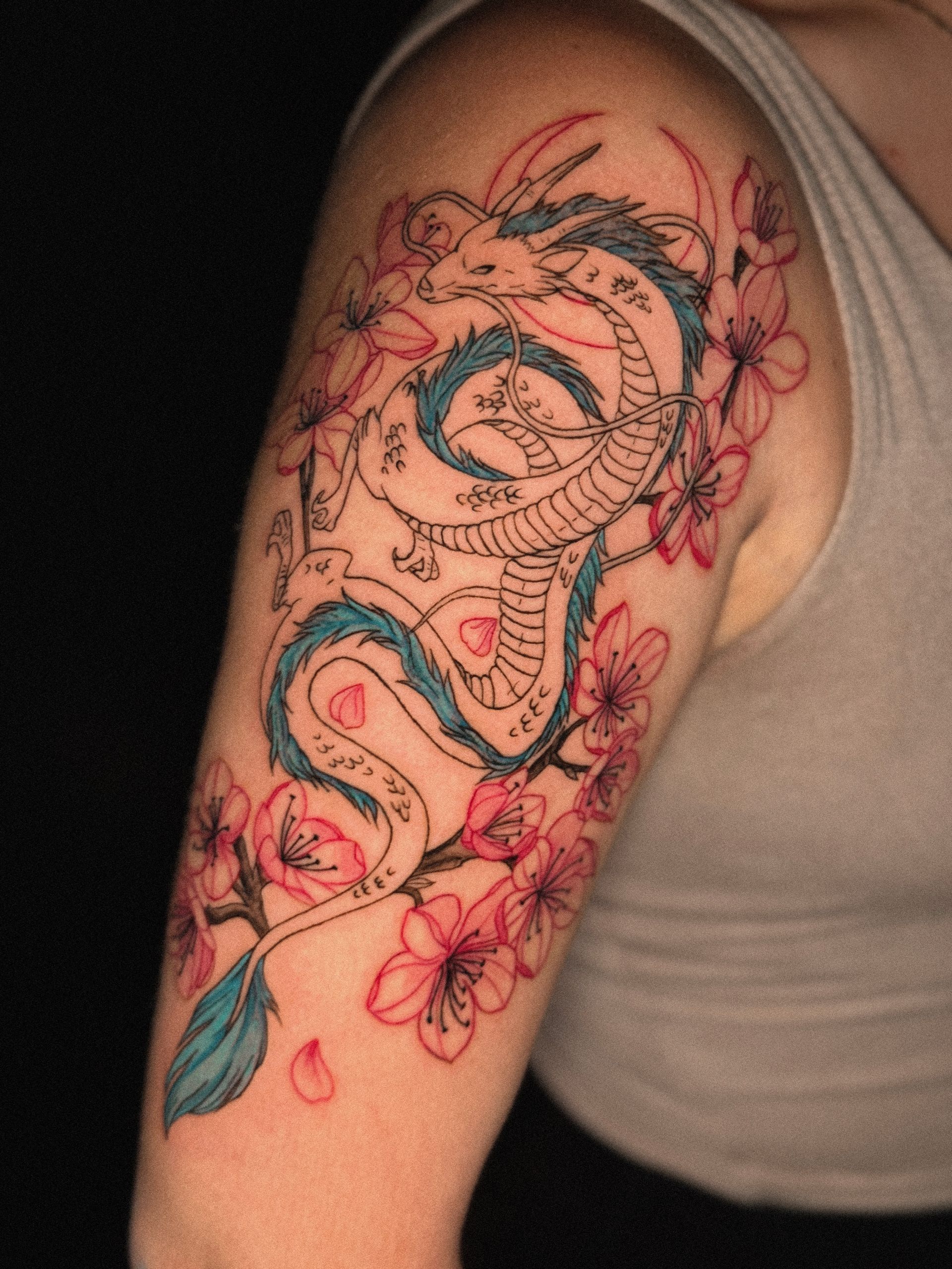 Dragon tattoo in blue, black, and pink with cherry blossoms on a woman's arm.