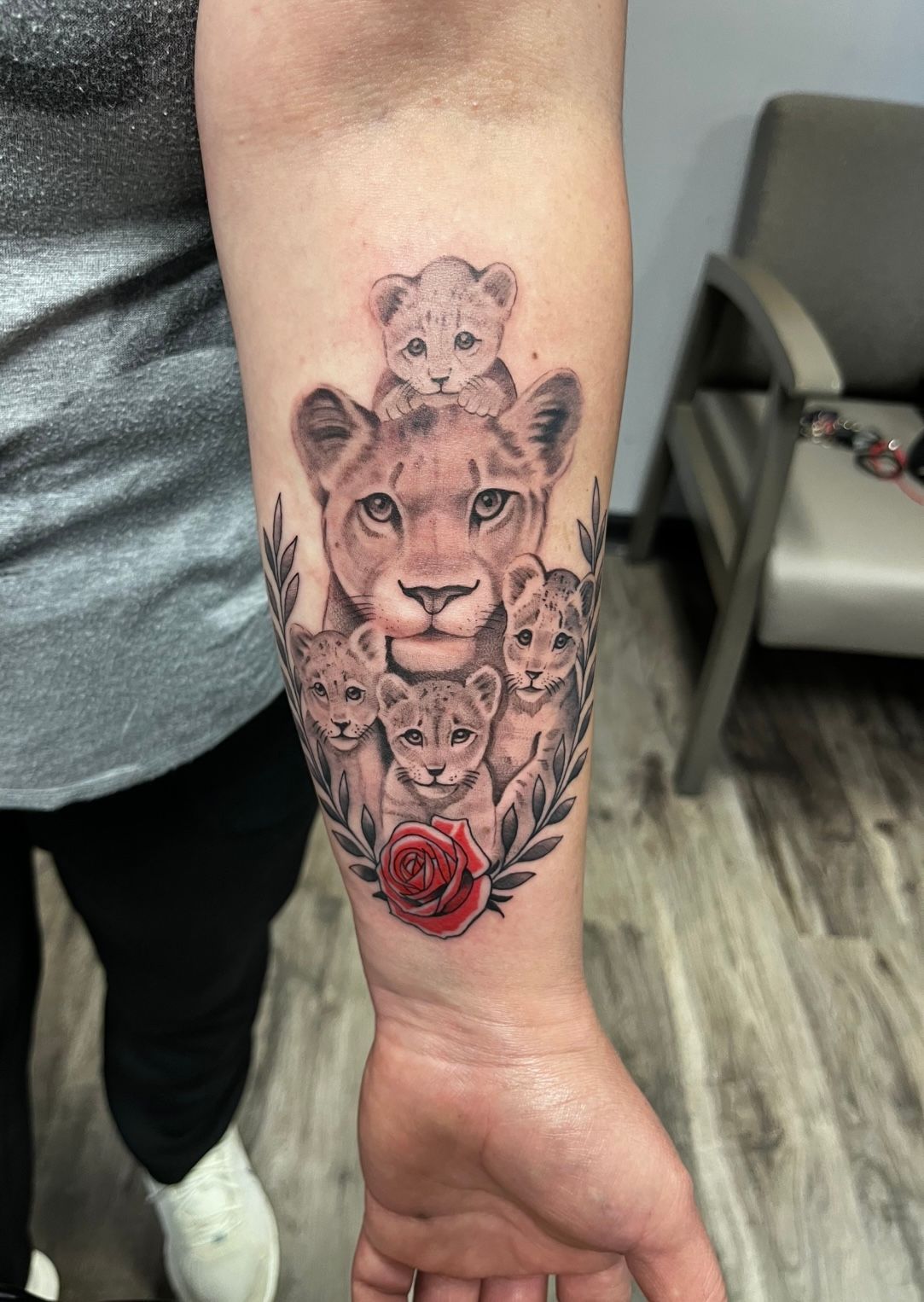 Lioness with cubs tattoo, with a red rose and laurel leaves on a forearm.