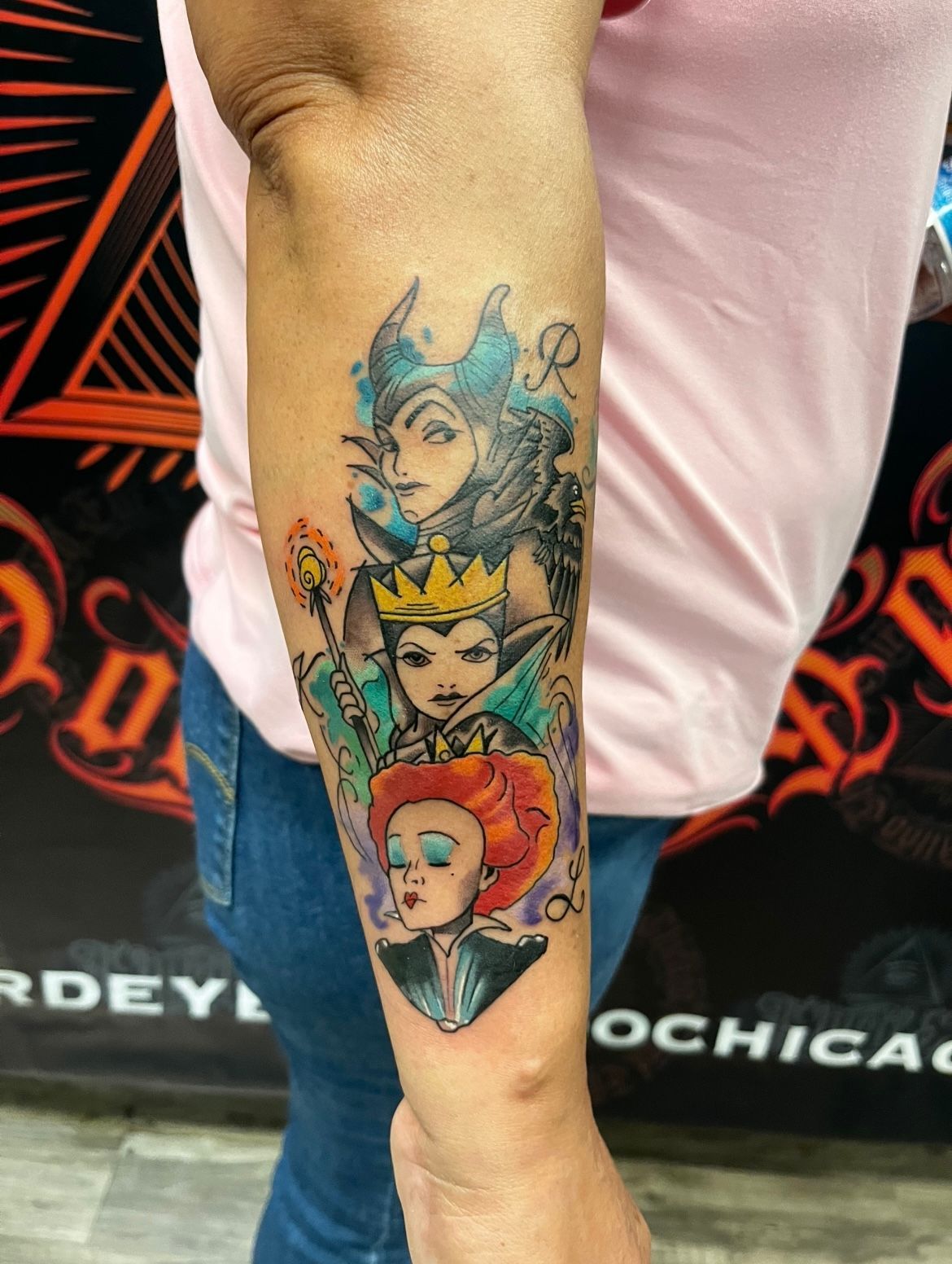Tattoo of Disney villains: Maleficent, Evil Queen, and Queen of Hearts on a person's arm.