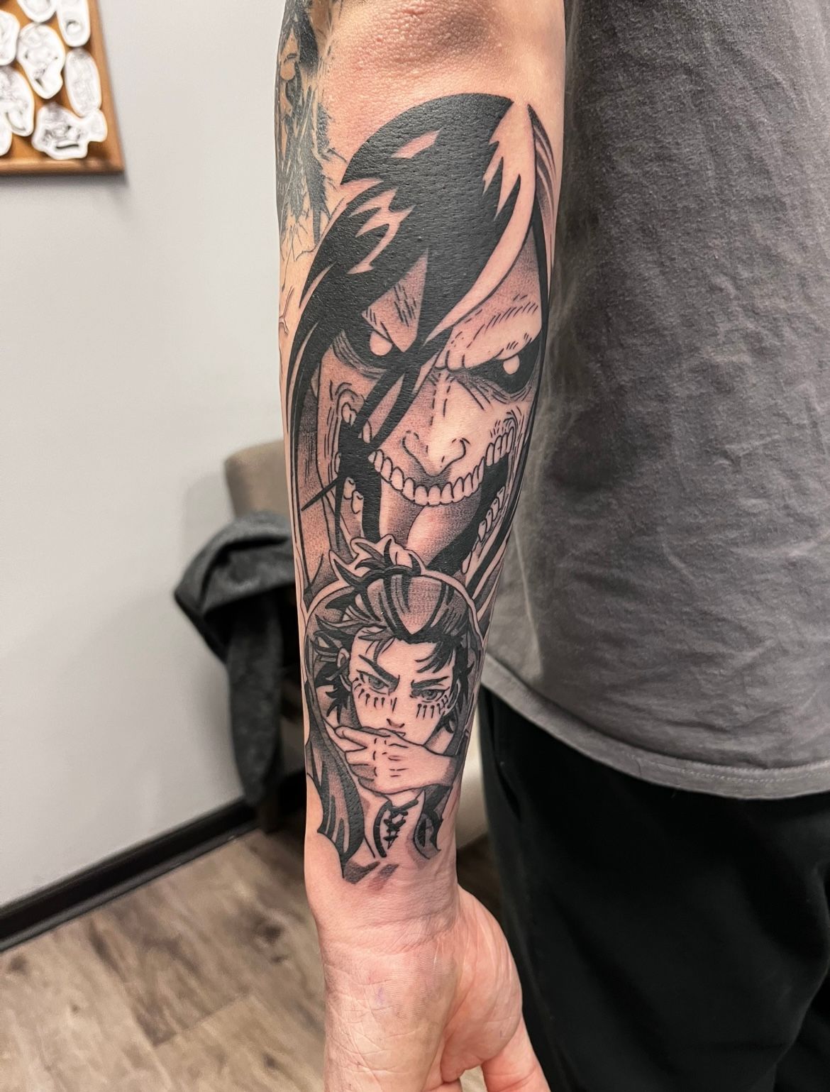 Tattoo of anime characters: Eren Yeager's Titan form above and a smaller character below, on a forearm.