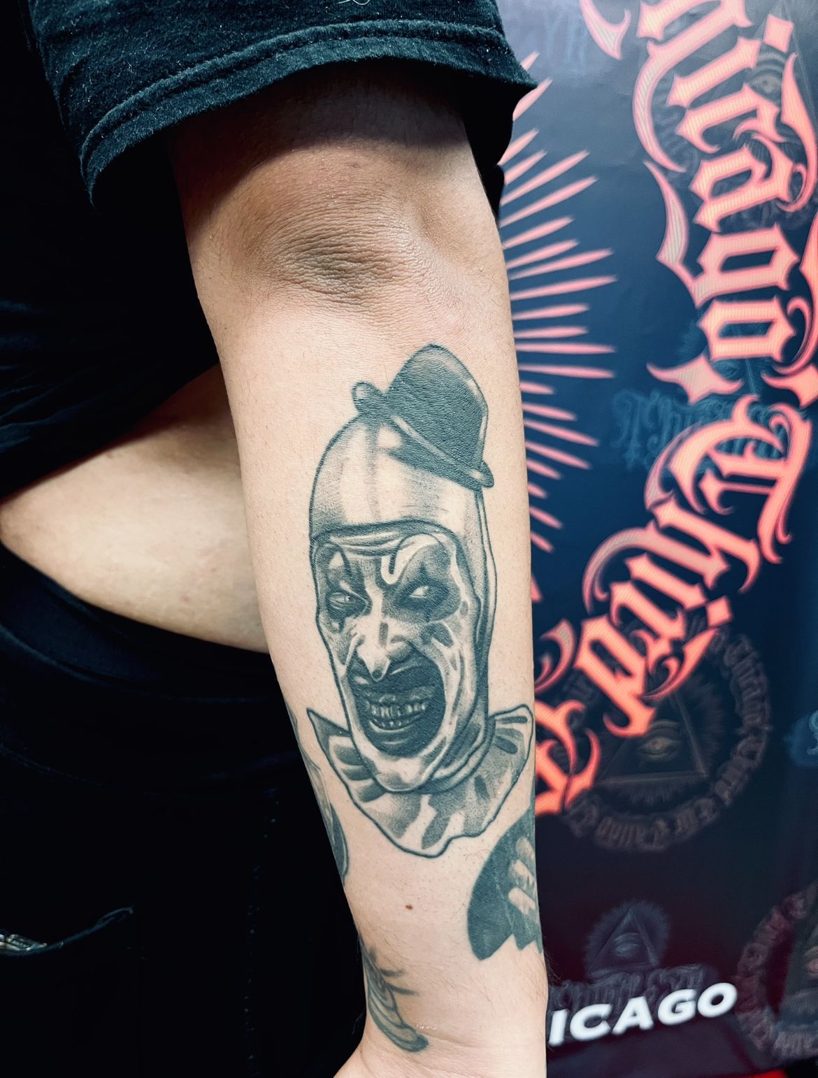 Black and white tattoo of a creepy clown face on a person's arm.