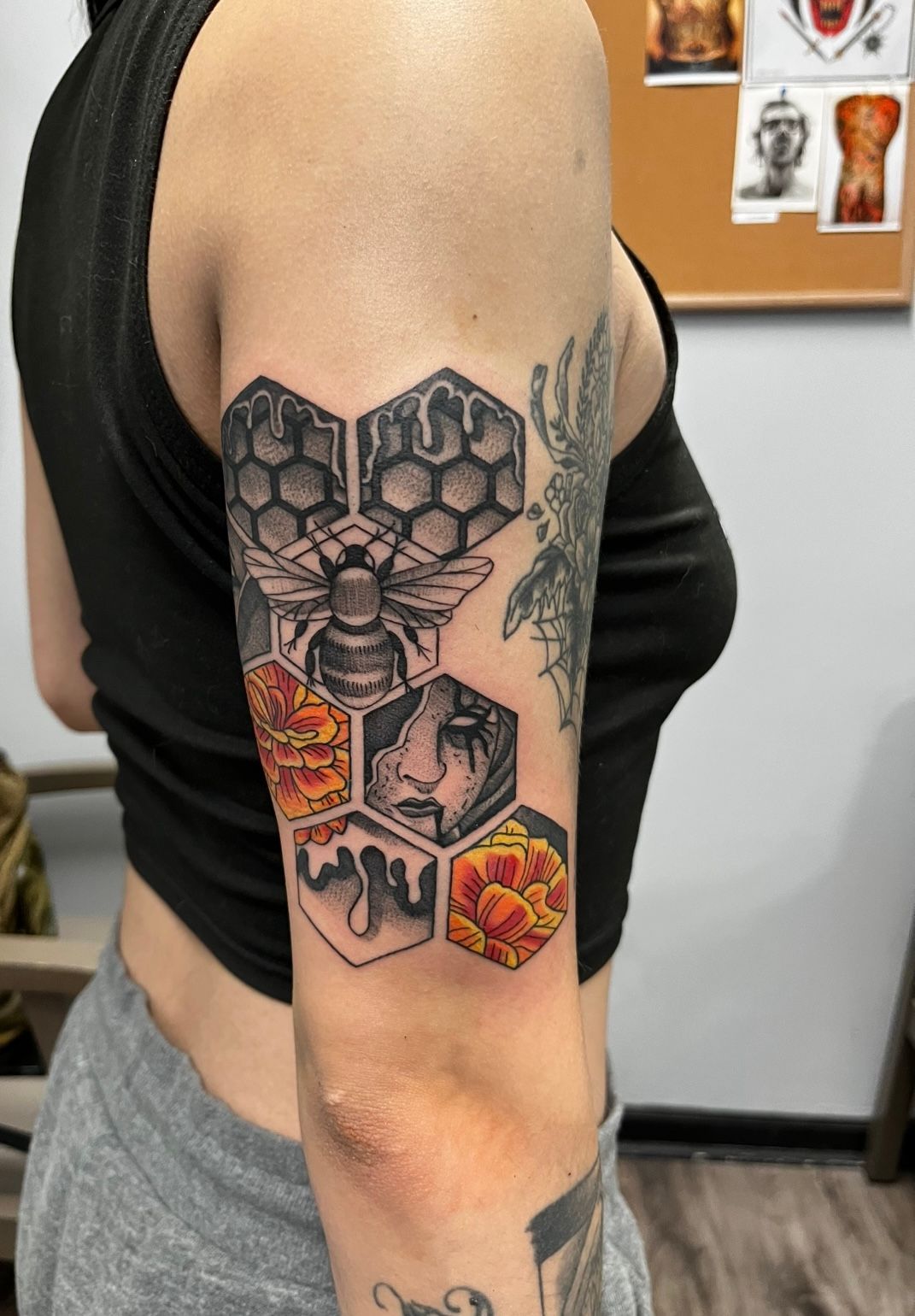 Tattoo of honeycomb with a bee, flowers, and a face on a woman's upper arm.
