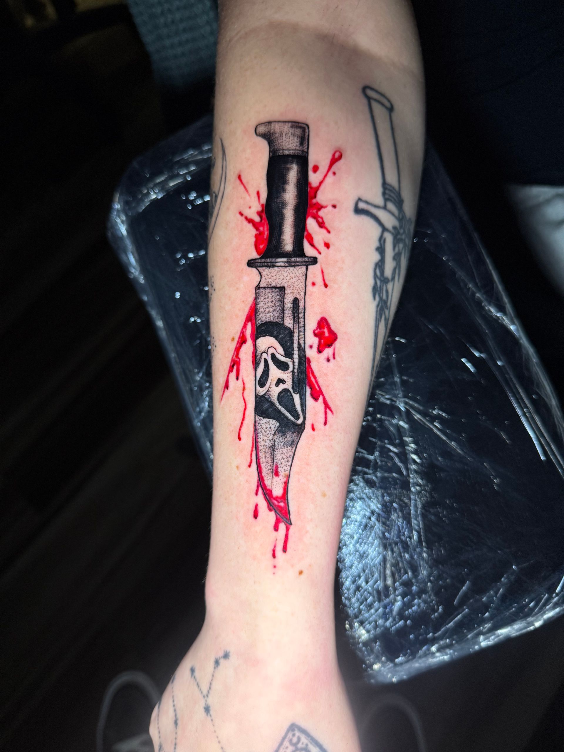 Tattoo of a knife with the Scream mask, red blood splatter.