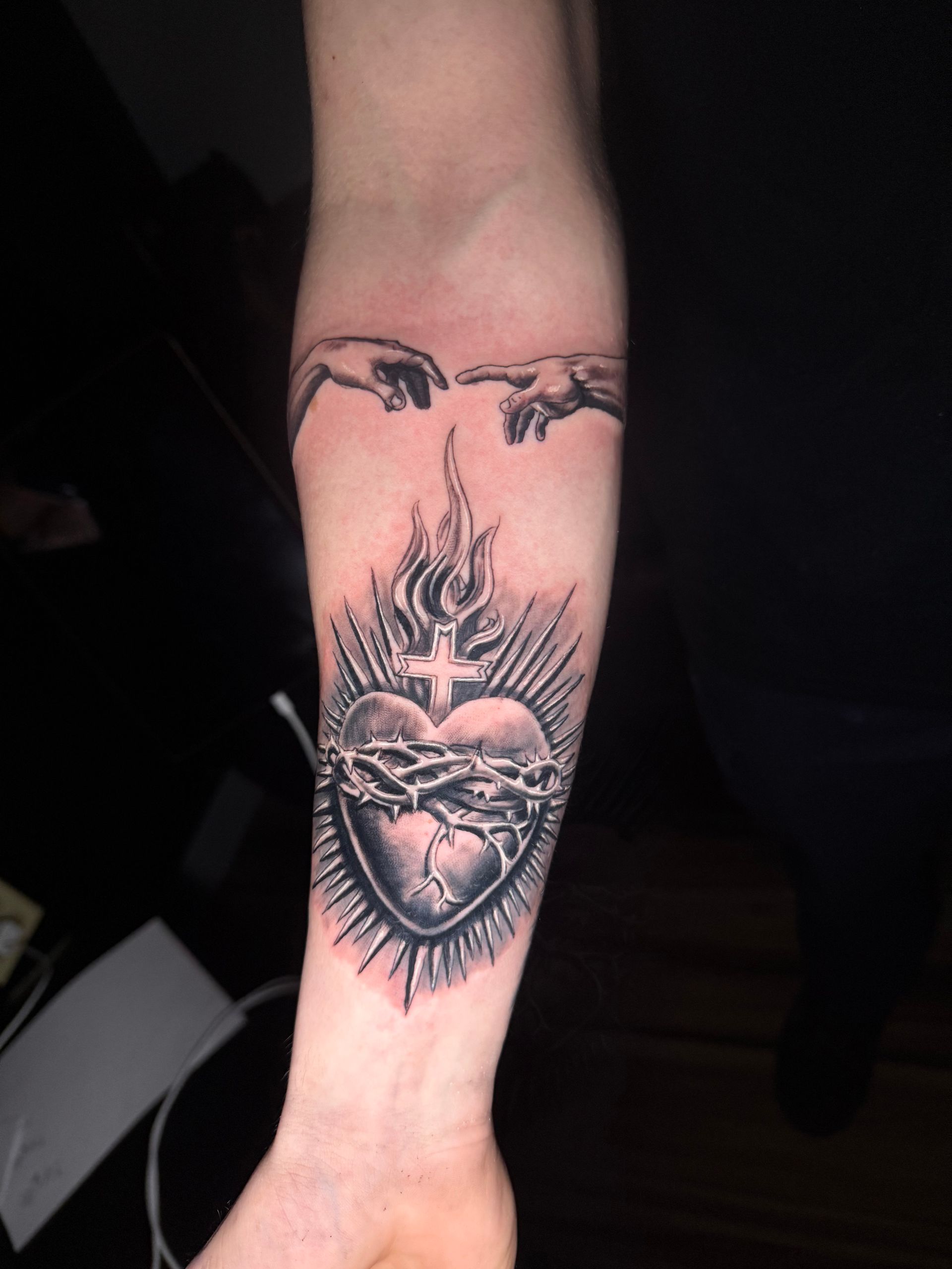 Tattoo of a flaming heart with a crown of thorns, a cross, and two hands reaching out from above.