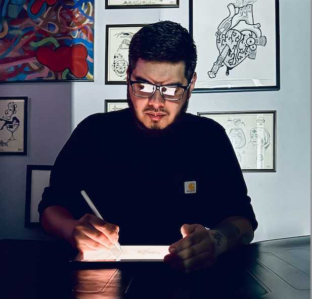 Man with glasses drawing on a light table. Artwork on the wall in the background.