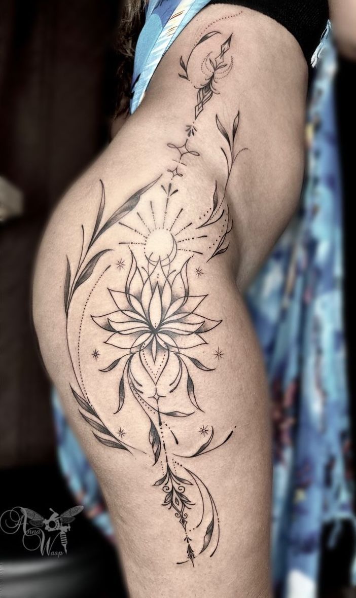 Black tattoo on hip; lotus flower with sun and vines.