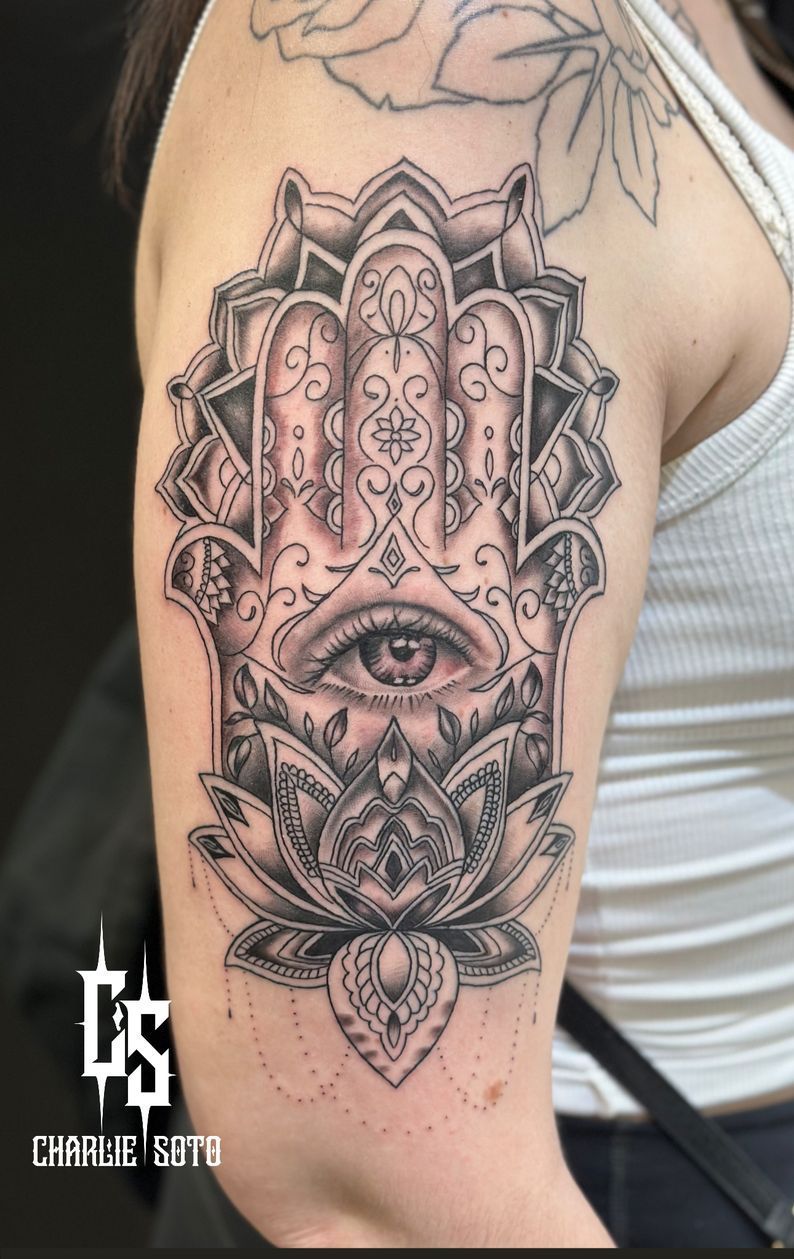 Black and white Hamsa hand tattoo with an eye, lotus, and ornate details on a person's arm.