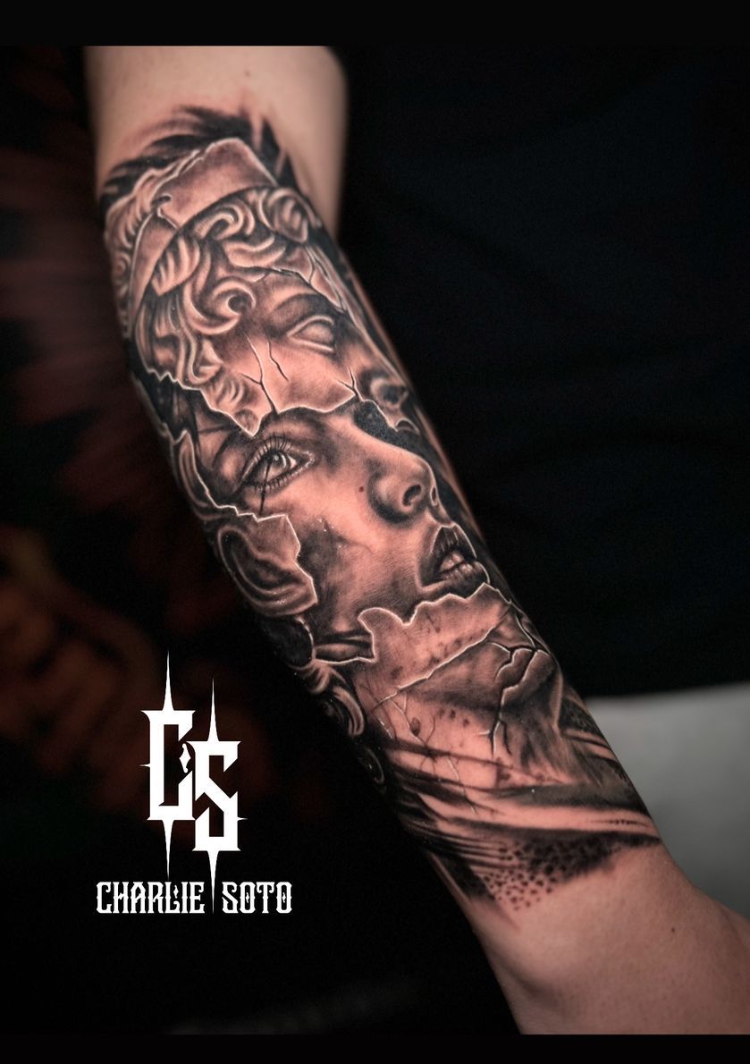 Black and grey arm tattoo of a fragmented classical bust, revealing a woman's face.