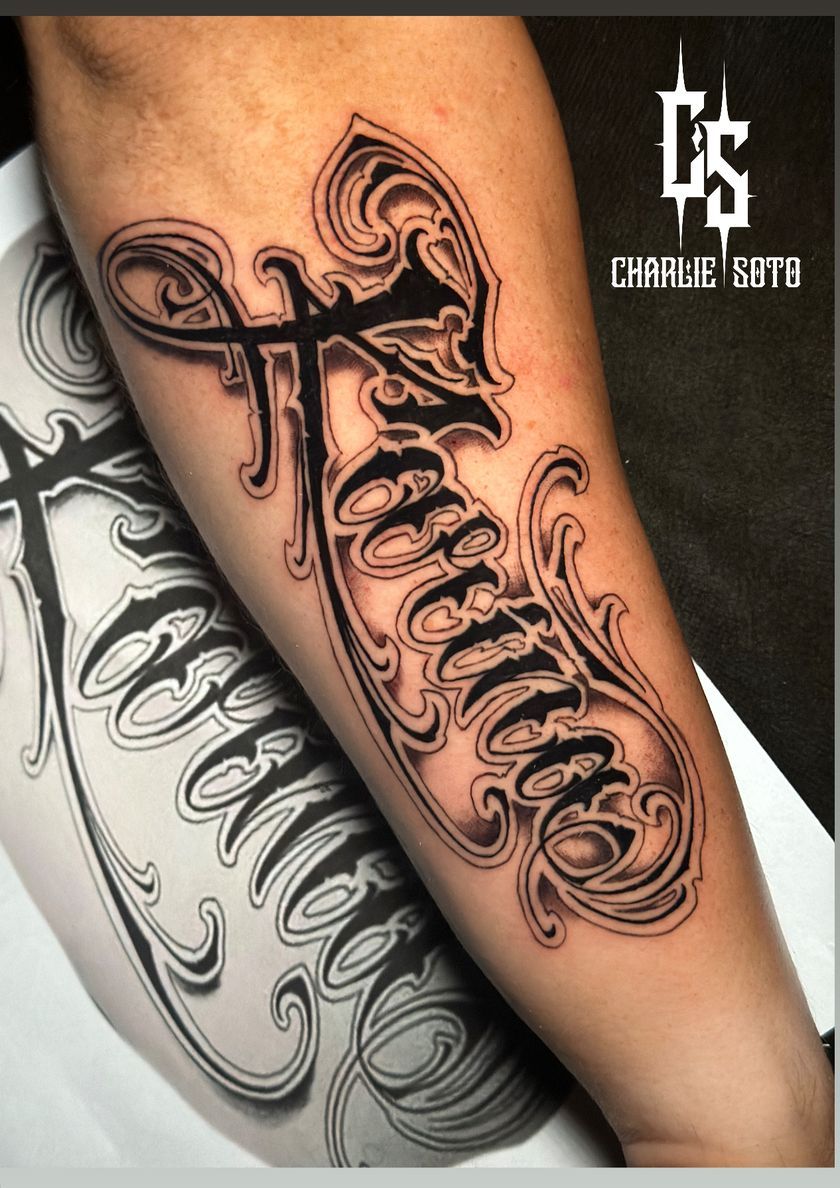 Black forearm tattoo with ornate script design.